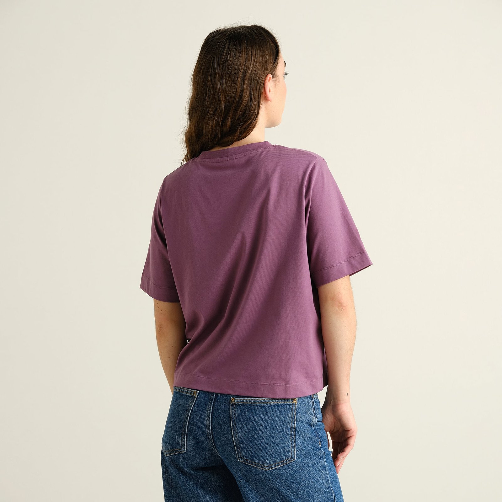 Back view of a model wearing the T-shirt Vadstena Base in Berry Purple with blue jeans.