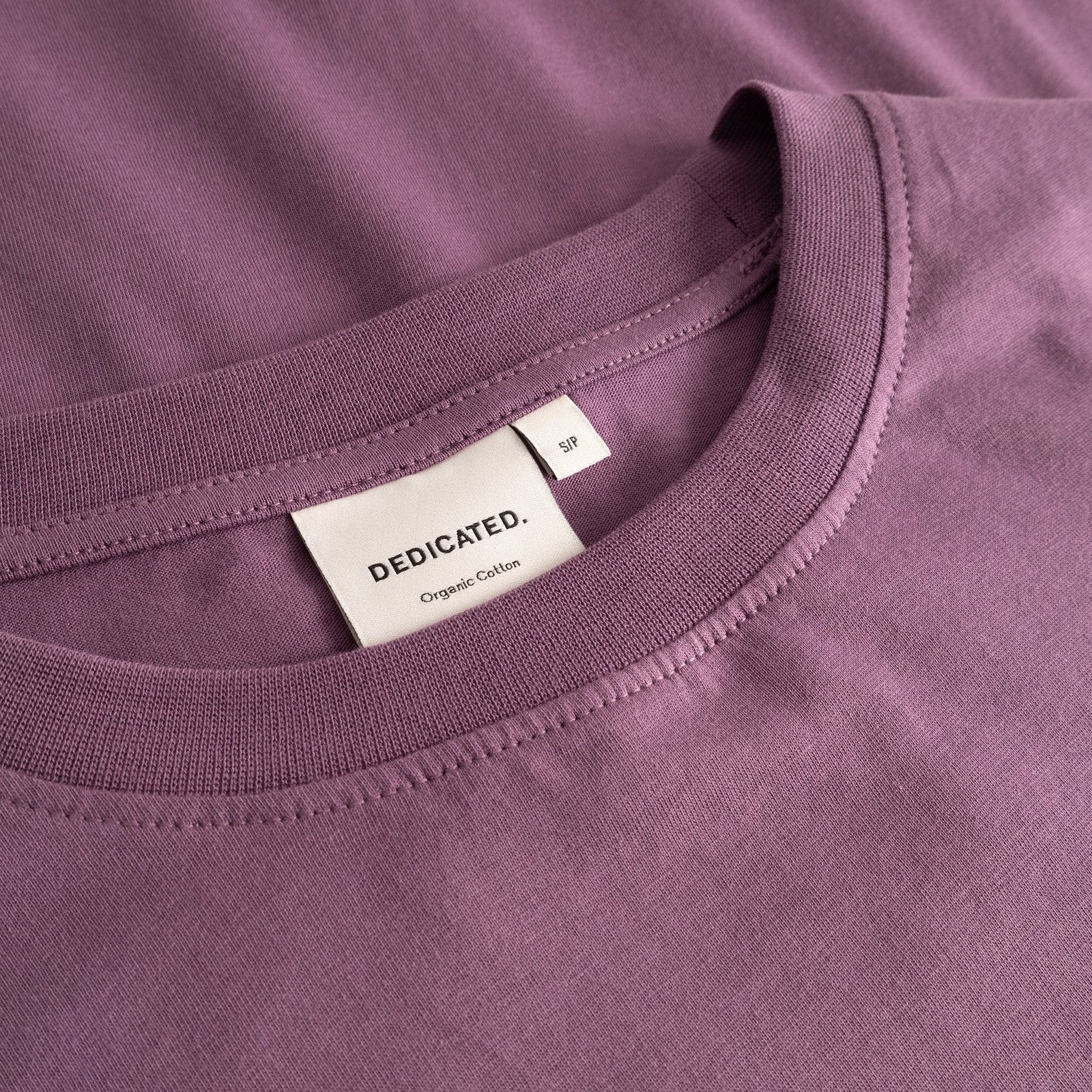 Detail shot of the organic cotton T-shirt Vadstena Base in Berry Purple, showing the soft ribbed collar and brand label.