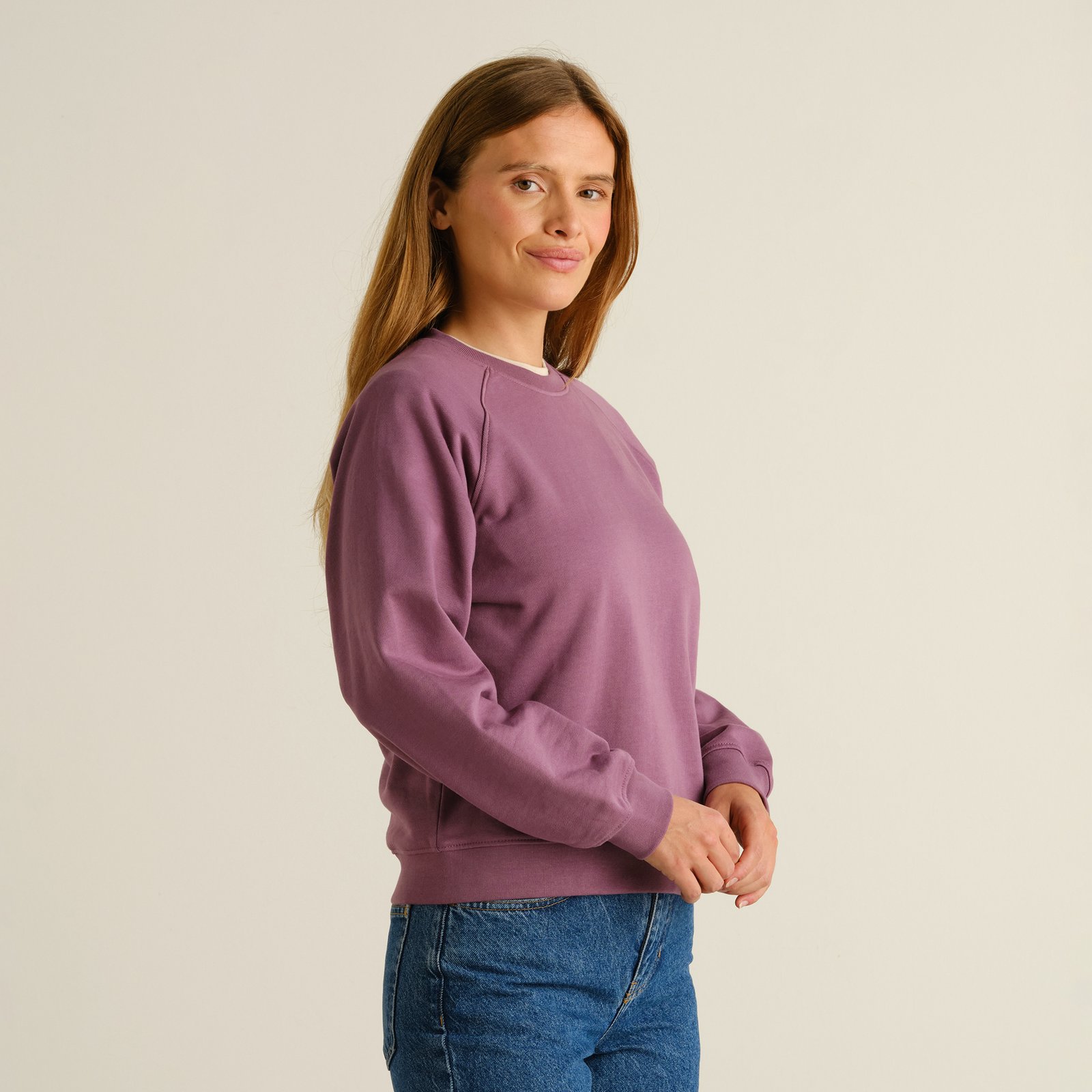 Side view of a woman wearing the Sweatshirt Ystad Base in a rich Berry Purple, paired with classic blue jeans.
