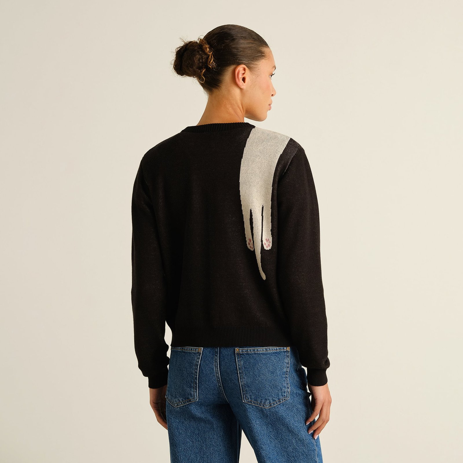 A woman shows off the back of the black Arendal sweater, featuring a playful, long cat's paw design over the shoulder.