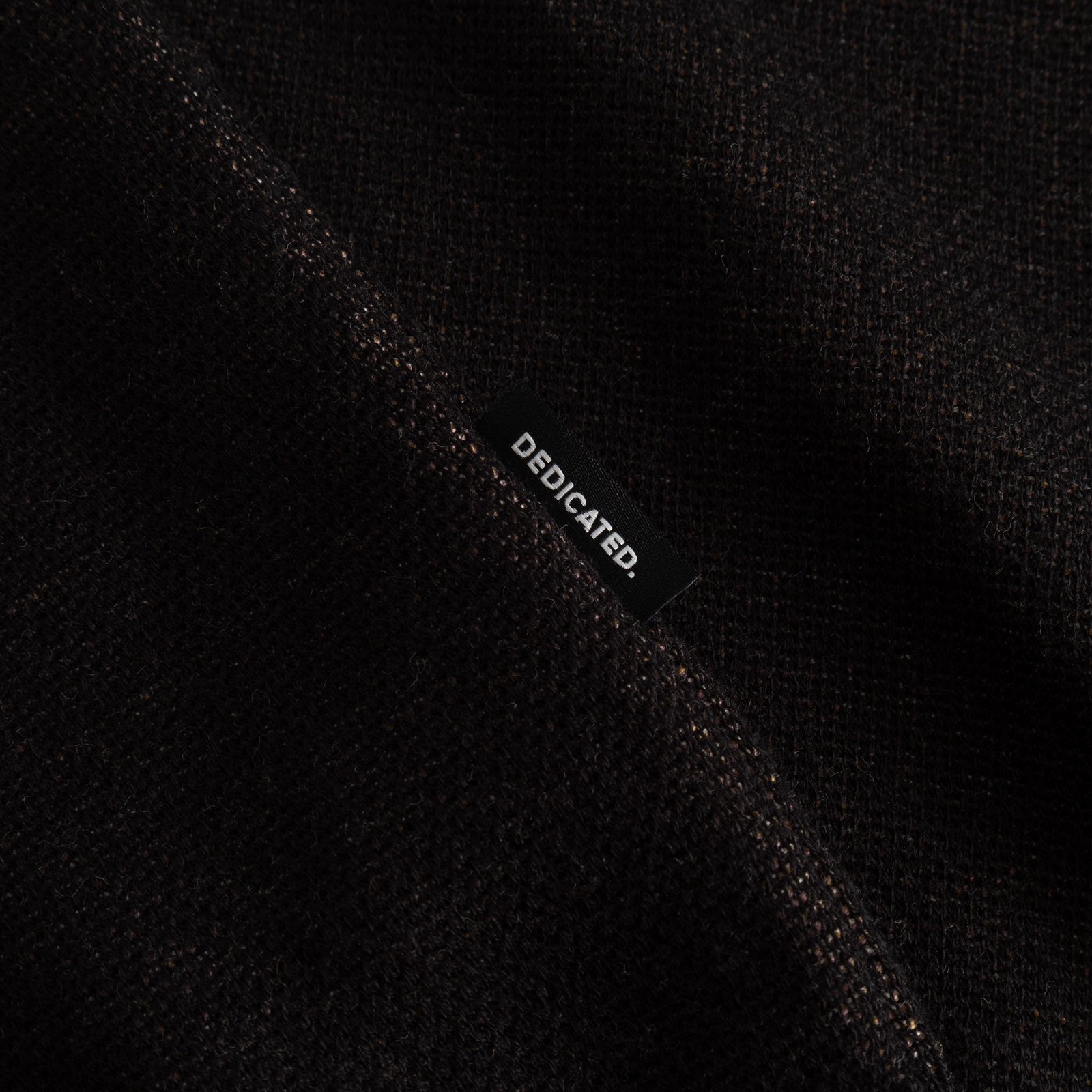 Close-up detail of the Sweater Arendal Long Cat in black, showcasing the jacquard knit texture and the Dedicated brand label.