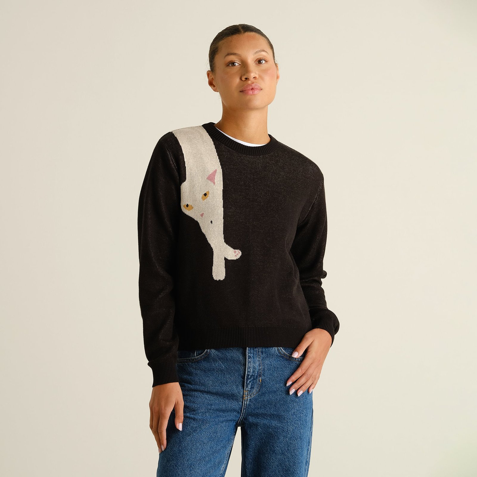 A woman models the black Arendal sweater featuring a playful long cat graphic, styled with classic blue jeans.