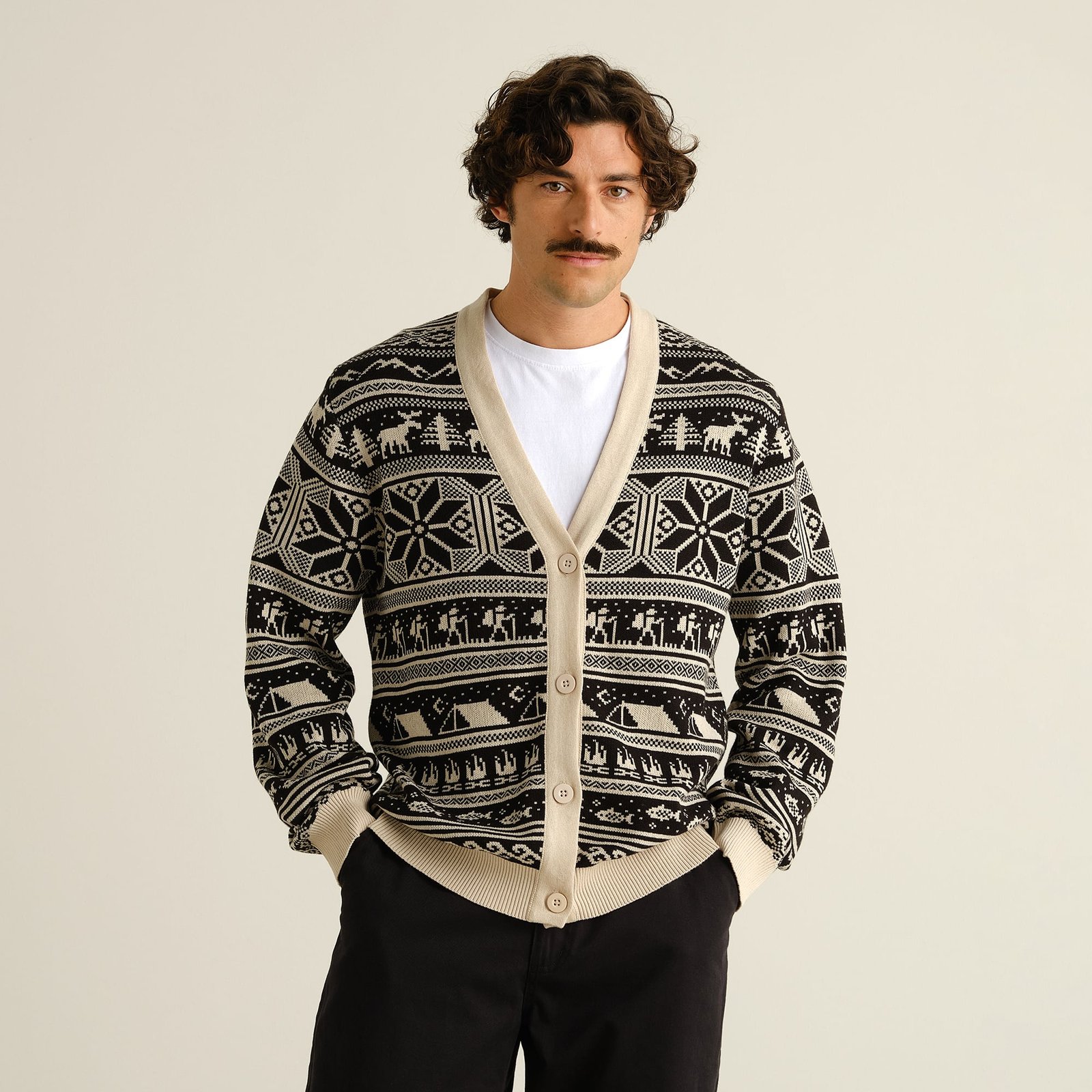 A man models the black and cream Delsbo cardigan, which features a fun Fair Isle pattern of hikers, tents, and snowflakes.