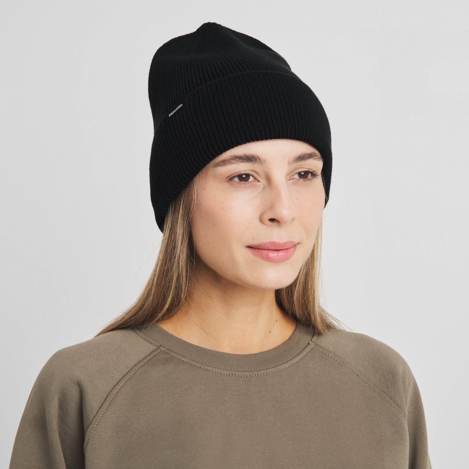 A woman models the classic black Beanie Hemavan, a chunky knit hat with a wide fold-up cuff, against a clean background.