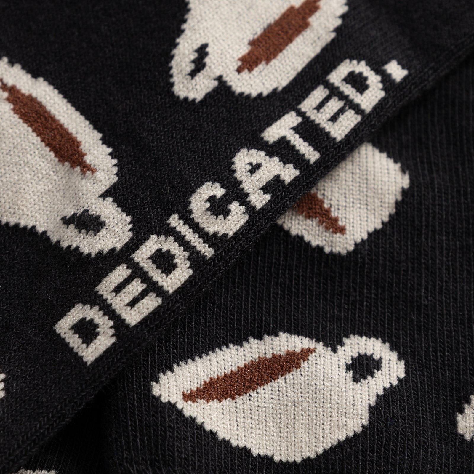 Close-up of the Sigtuna socks in black, showing the detailed coffee cup pattern and the knitted DEDICATED. logo.
