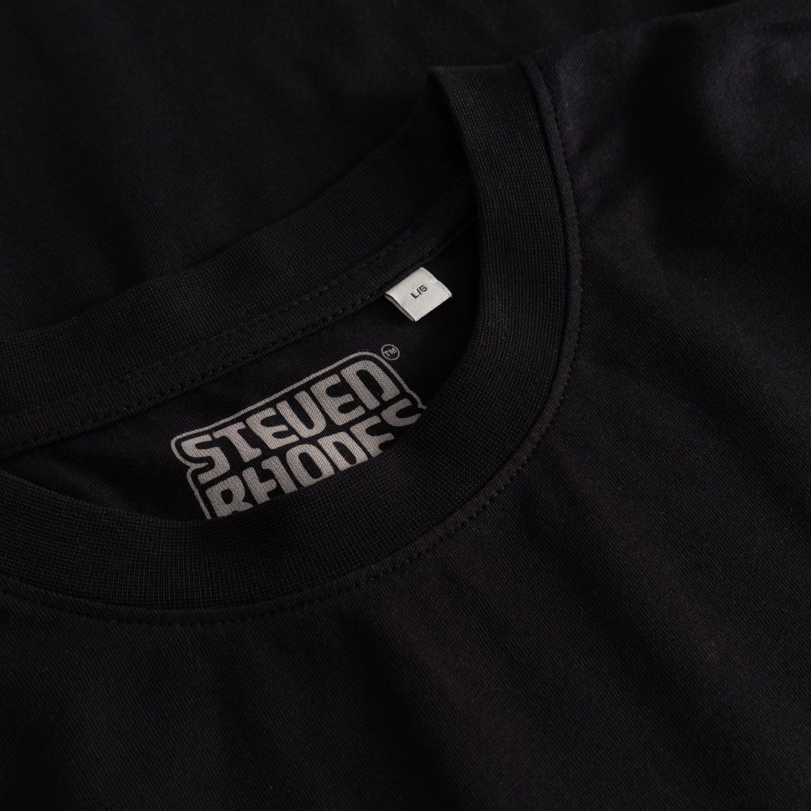 Close-up of the ribbed collar of the black Stockholm T-shirt, showing the Steven Rhodes logo printed inside the neck.