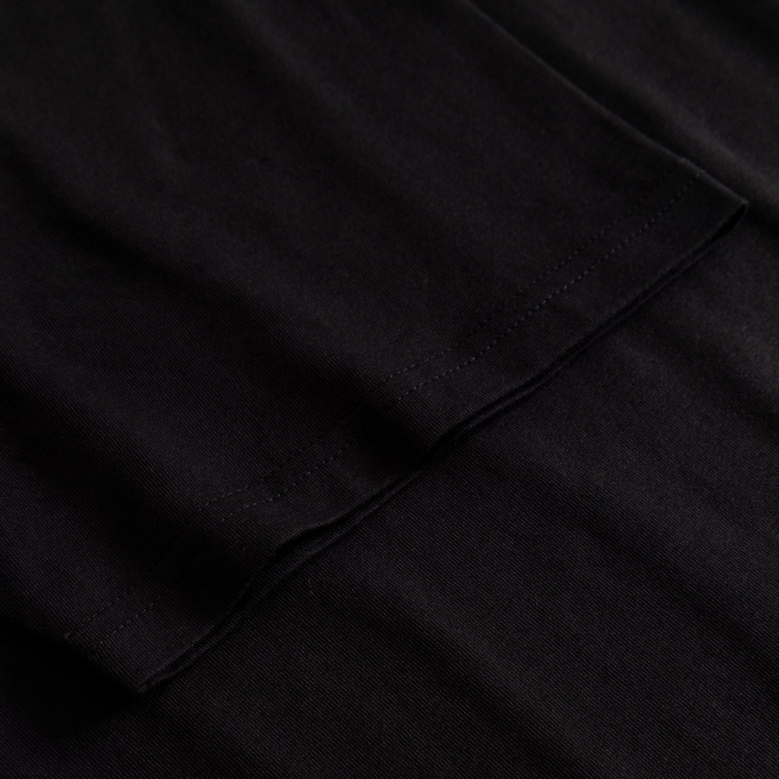 A close-up of the sleeve and stitching detail on the black T-shirt Stockholm Worship Coffee.