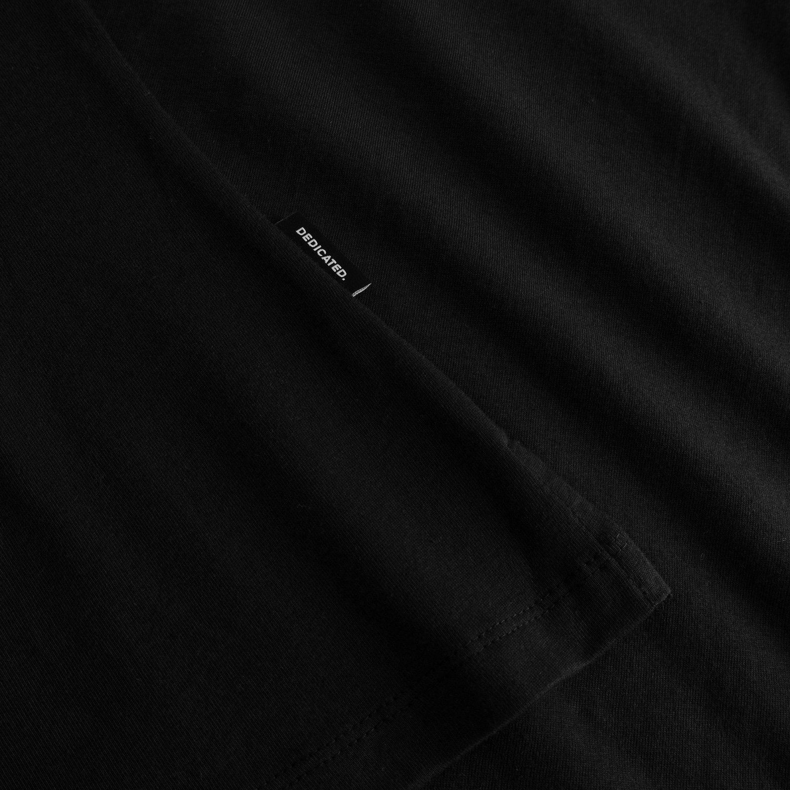 A detailed close-up of the black Visby Painted Bird T-shirt, highlighting the sleeve's texture and the classic Dedicated tag.