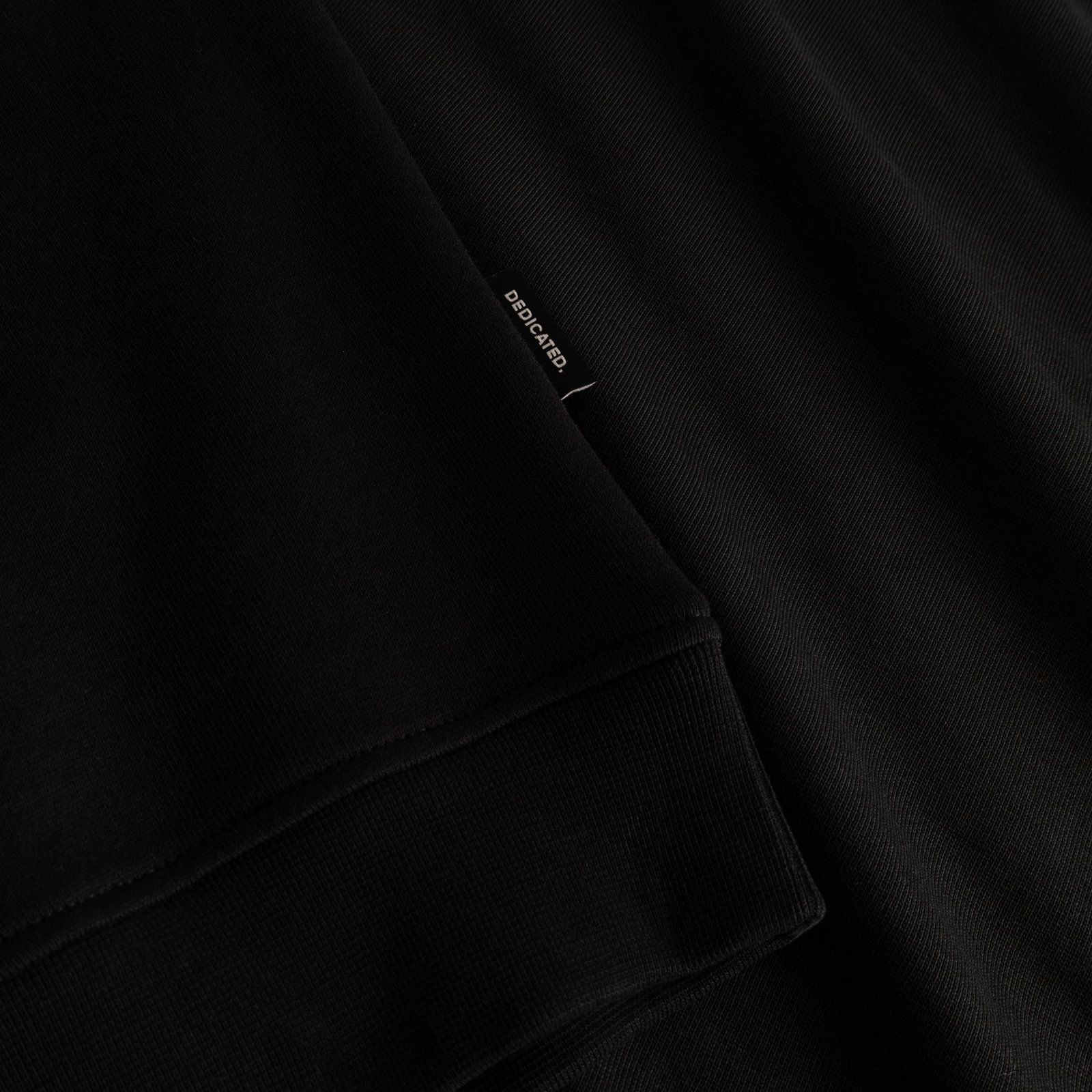 A close-up of the Sweatshirt Ystad in black, highlighting the soft ribbed sleeve cuff and the discreet Dedicated brand tag.