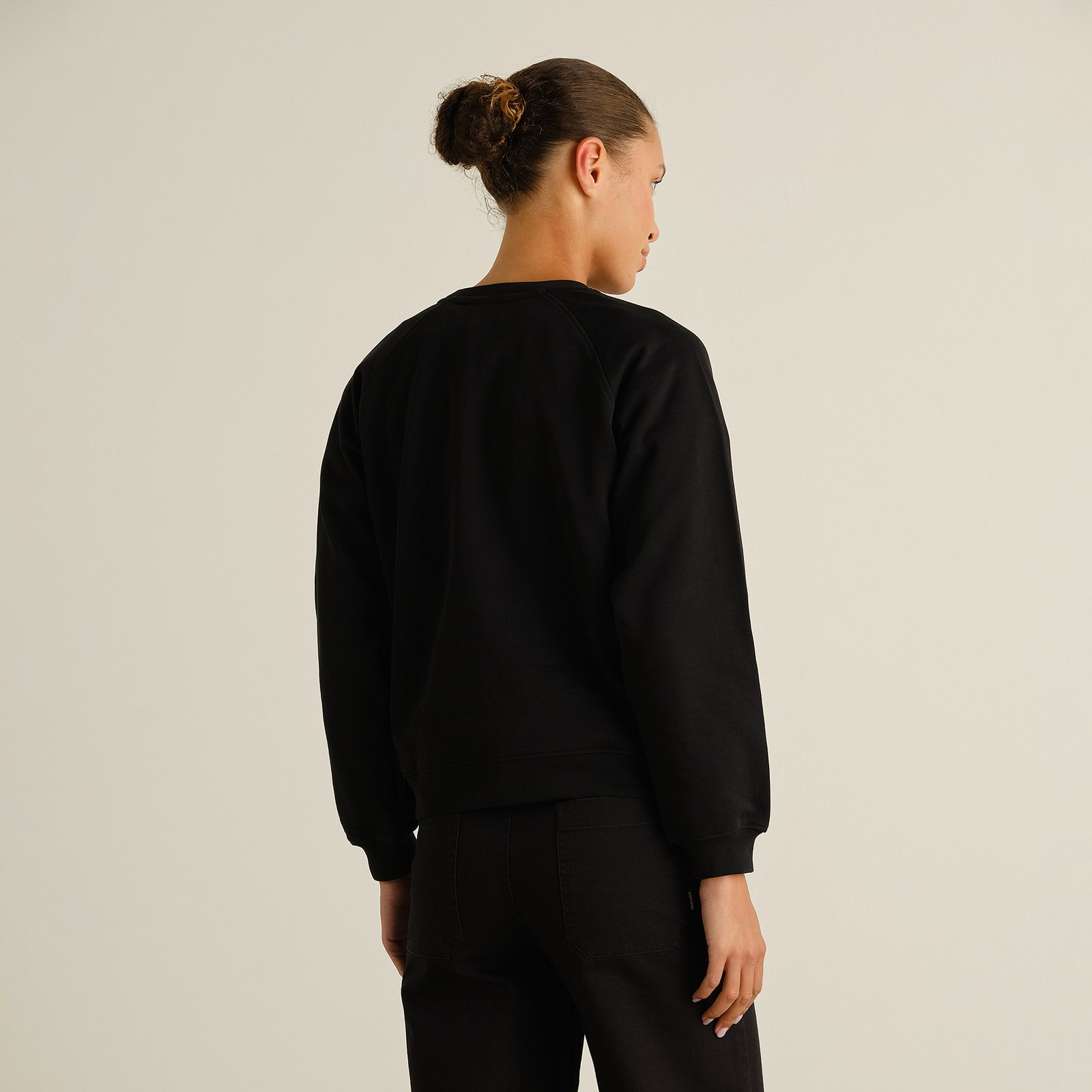 A model wearing the black Sweatshirt Ystad Painted Swans, seen from the back to showcase the fit and raglan sleeves.