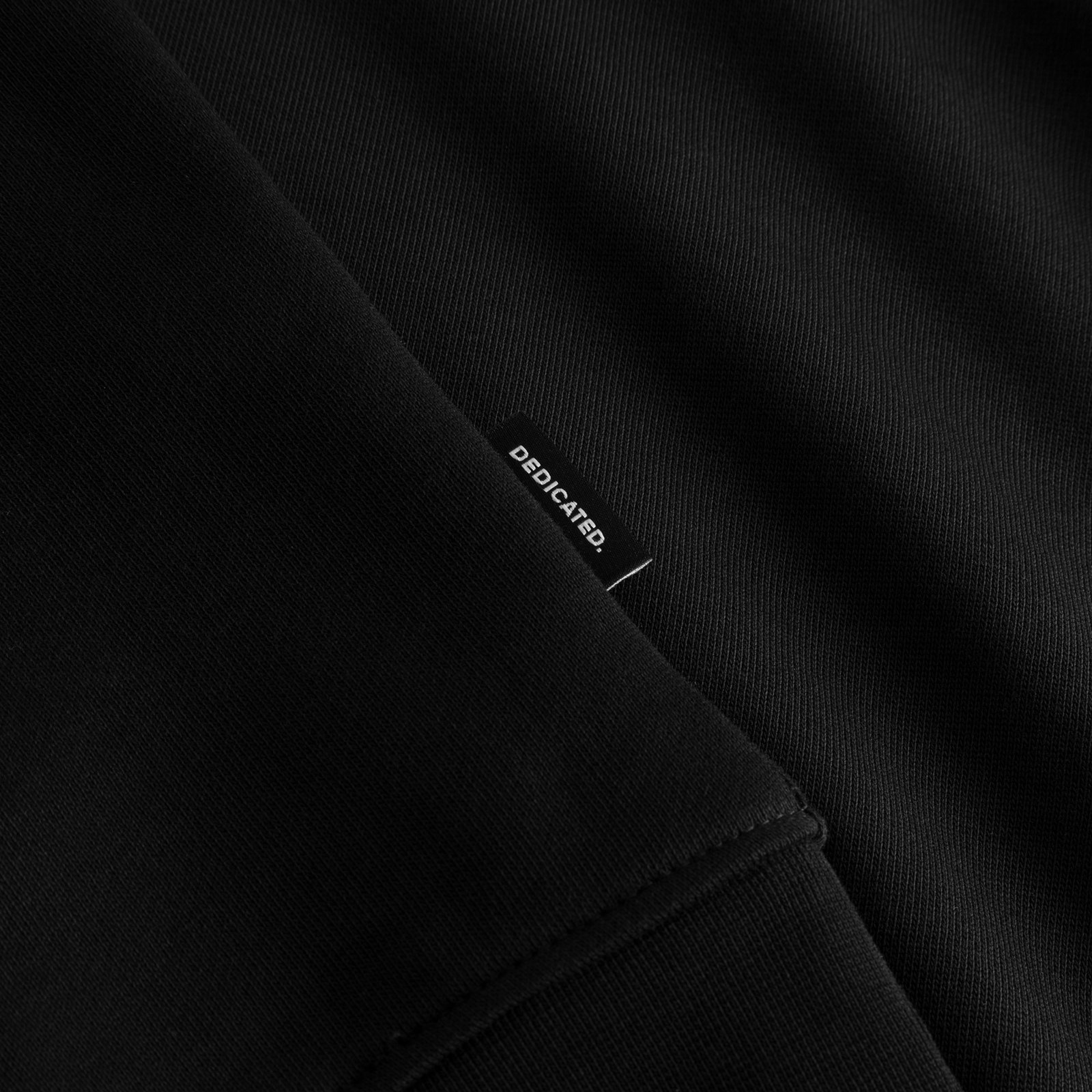 Close-up detail of the Sweatshirt Ystad Painted Swans in black, highlighting the small Dedicated brand tag.
