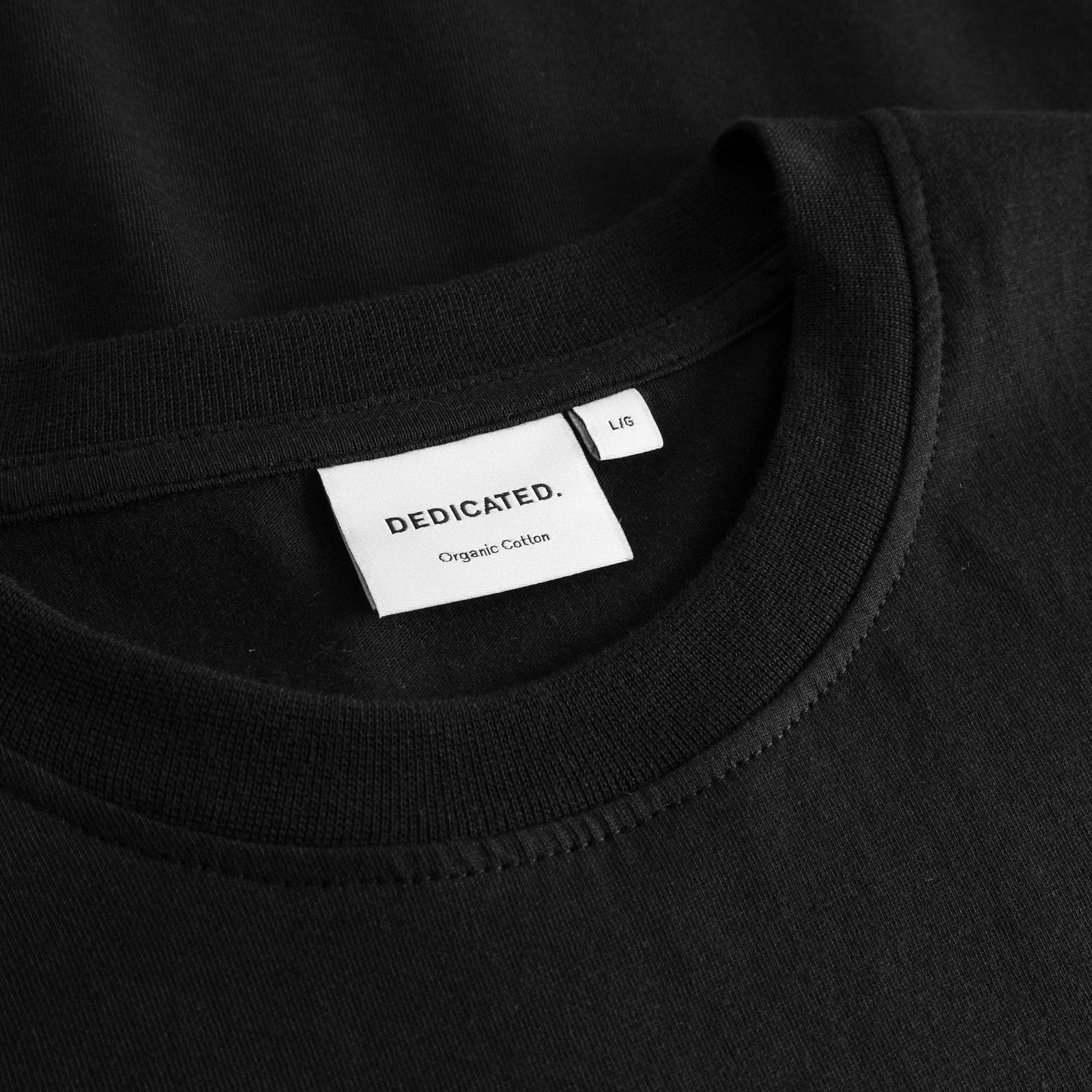 Close-up of the Dedicated label and ribbed crew neck on the black T-shirt Stockholm Apres Ski Instructor.