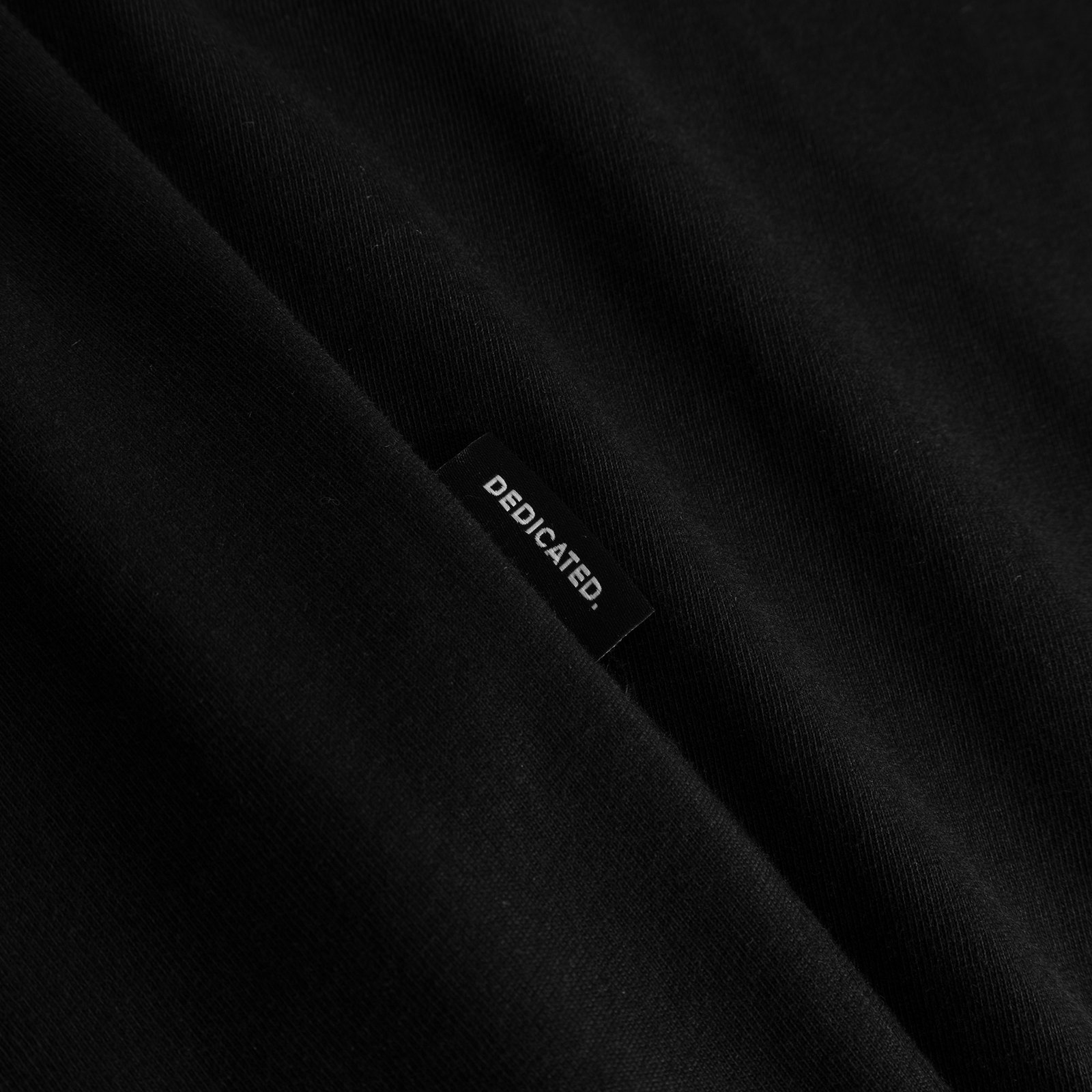 Close-up of the woven Dedicated brand tab on the black T-shirt Stockholm Painted Side Bike.