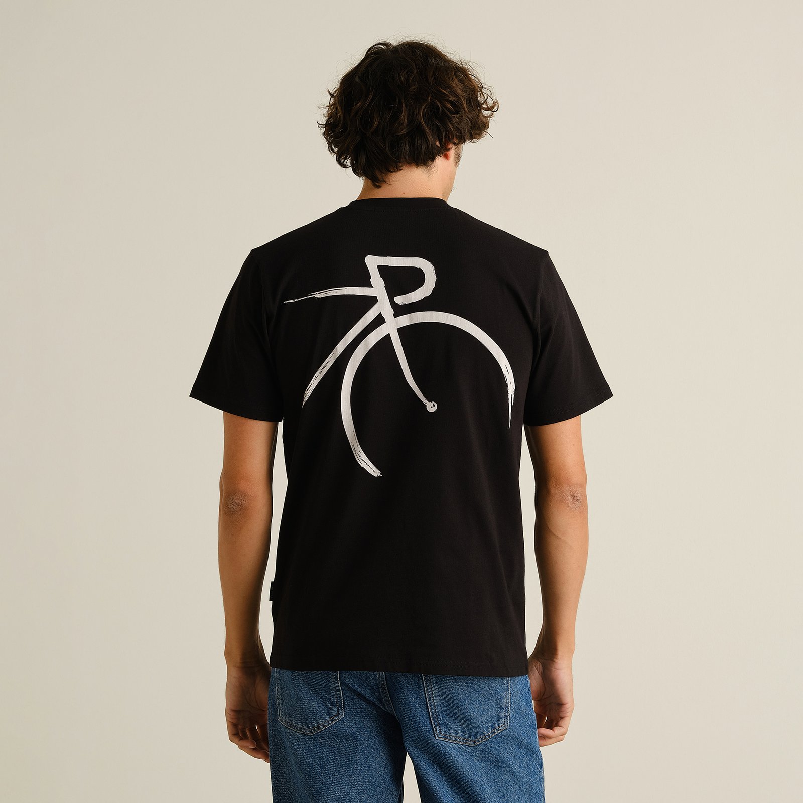 A guy showing off the back of the black T-shirt Stockholm, featuring a cool, painted-style bicycle graphic.