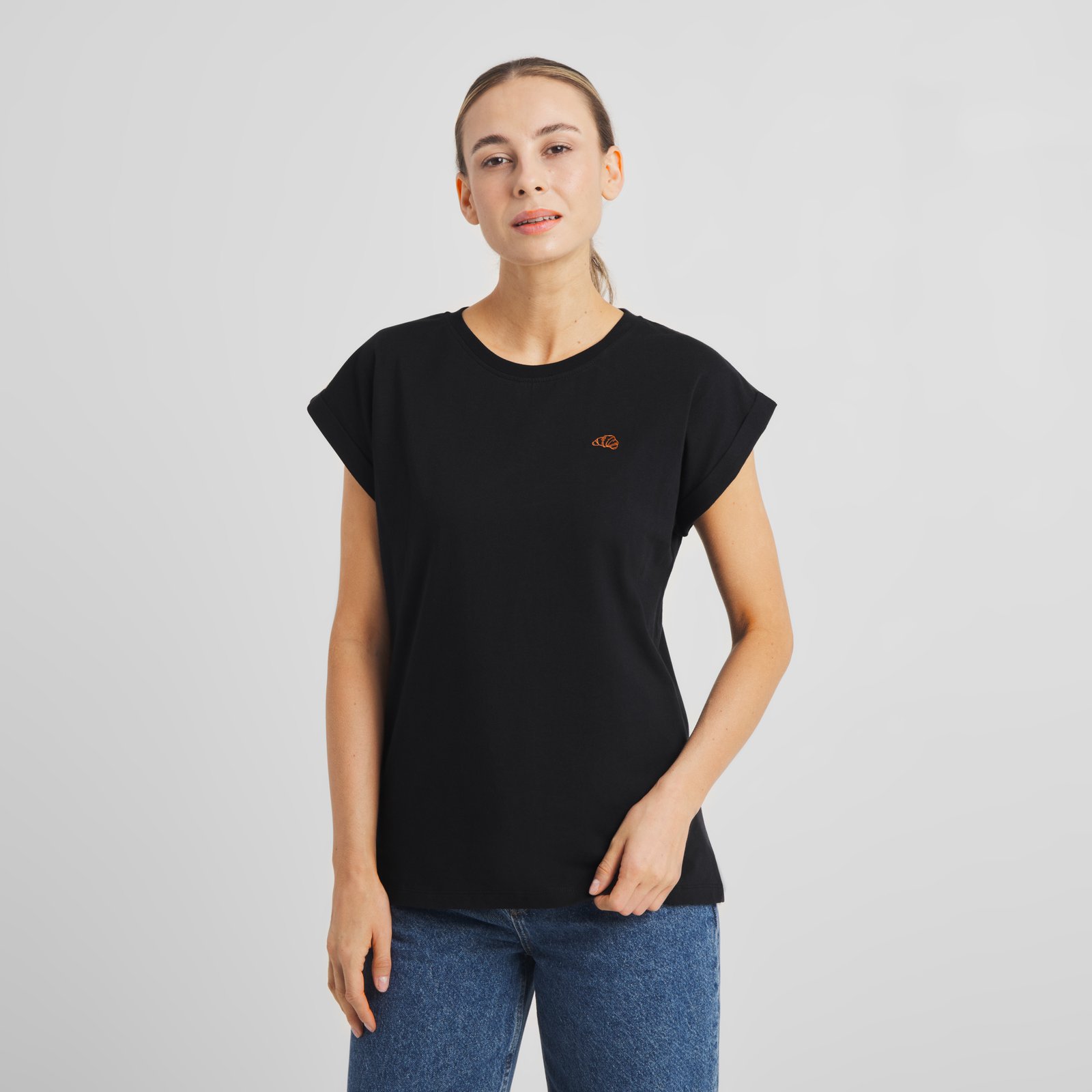 A woman models the black T-shirt Visby, which features a small embroidered croissant on the chest.