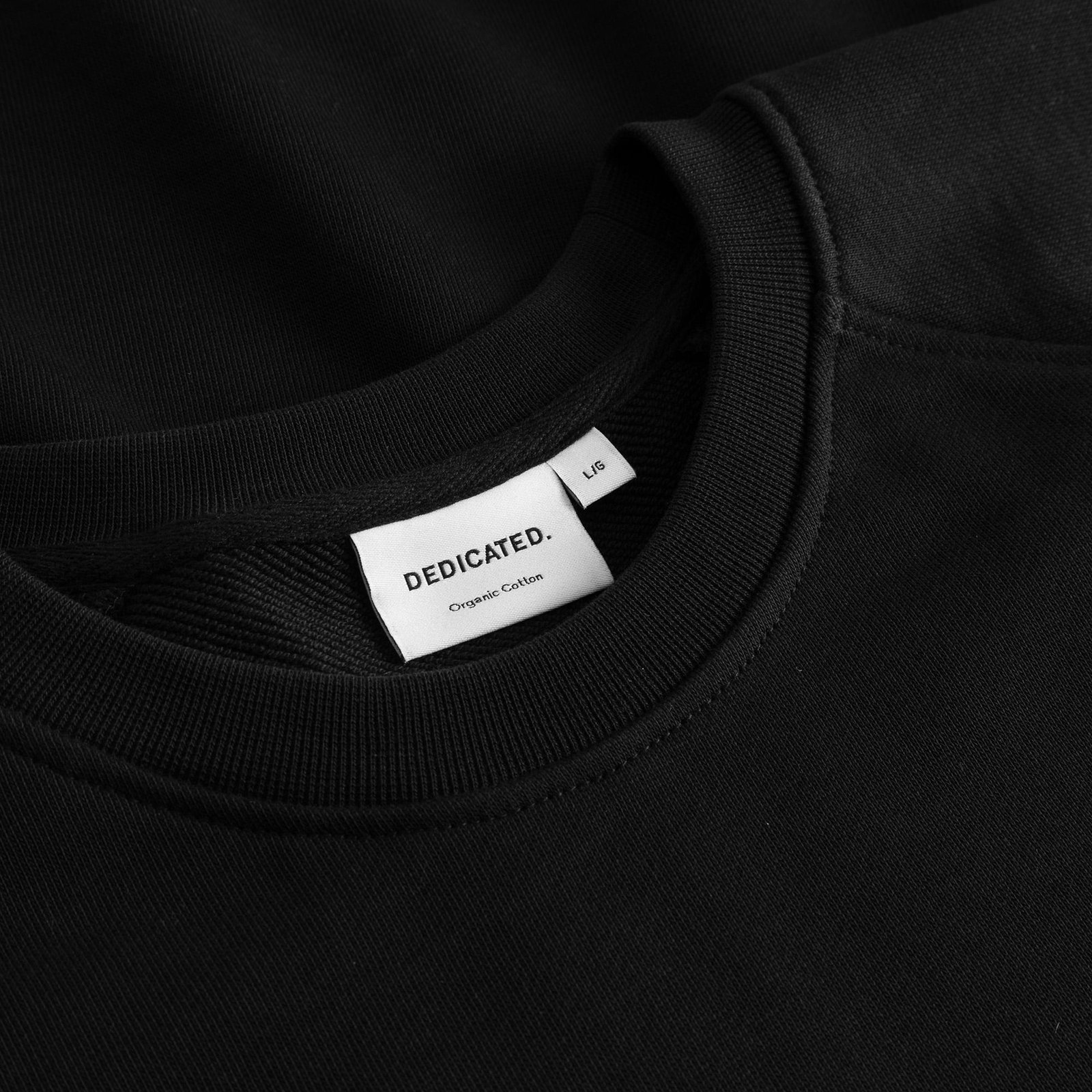 A detailed close-up of the ribbed crewneck on the black Sweatshirt Malmoe, showing the 'Dedicated' brand label.