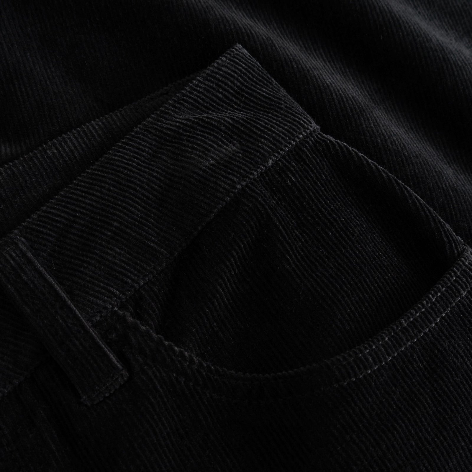 Eine Detailaufnahme der schwarzen Cordhose Ryda, die die Textur des Stoffes und die Vordertasche hervorhebt.