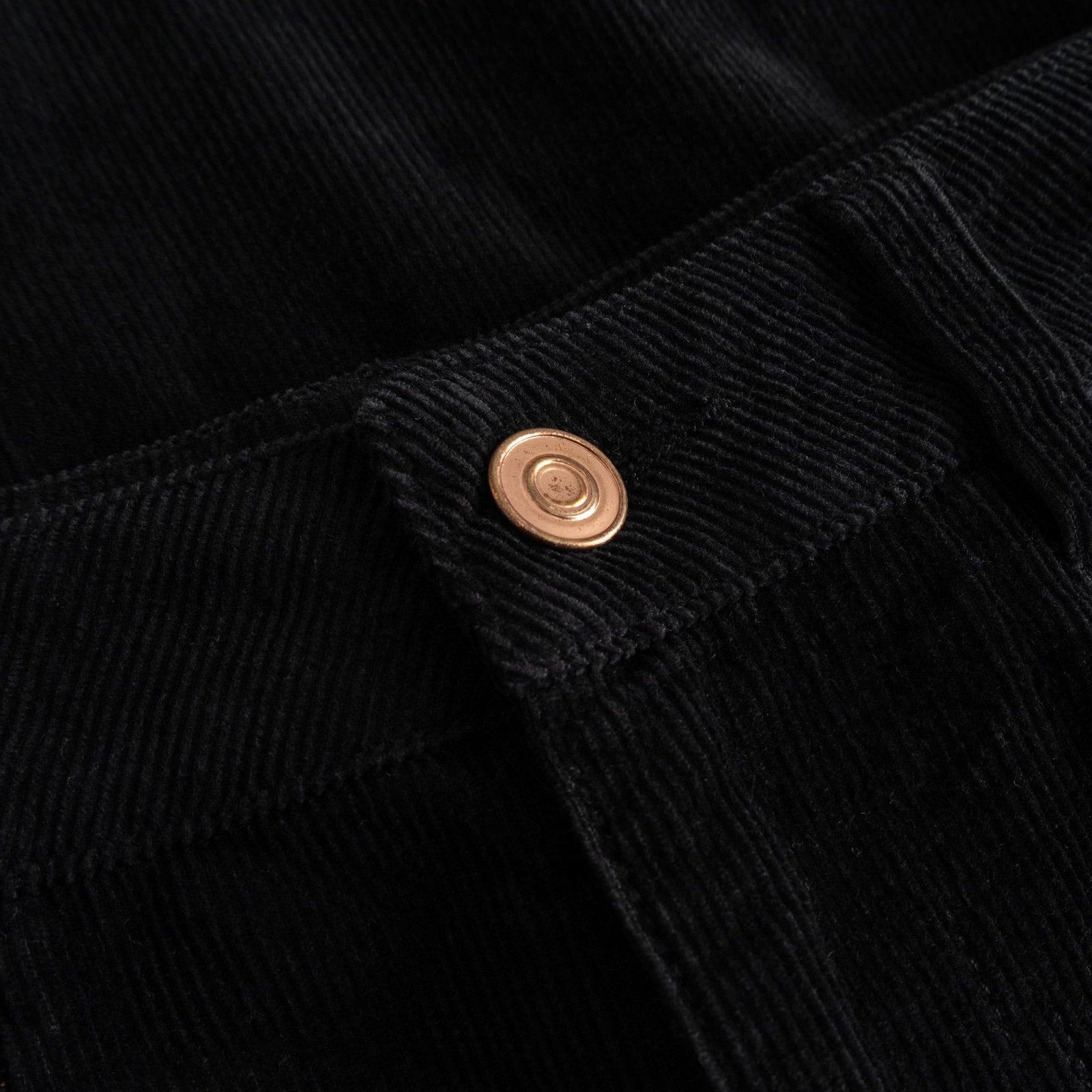 Detailansicht des Metallknopfs am Hosenbund der schwarzen Cordhose Ryda.