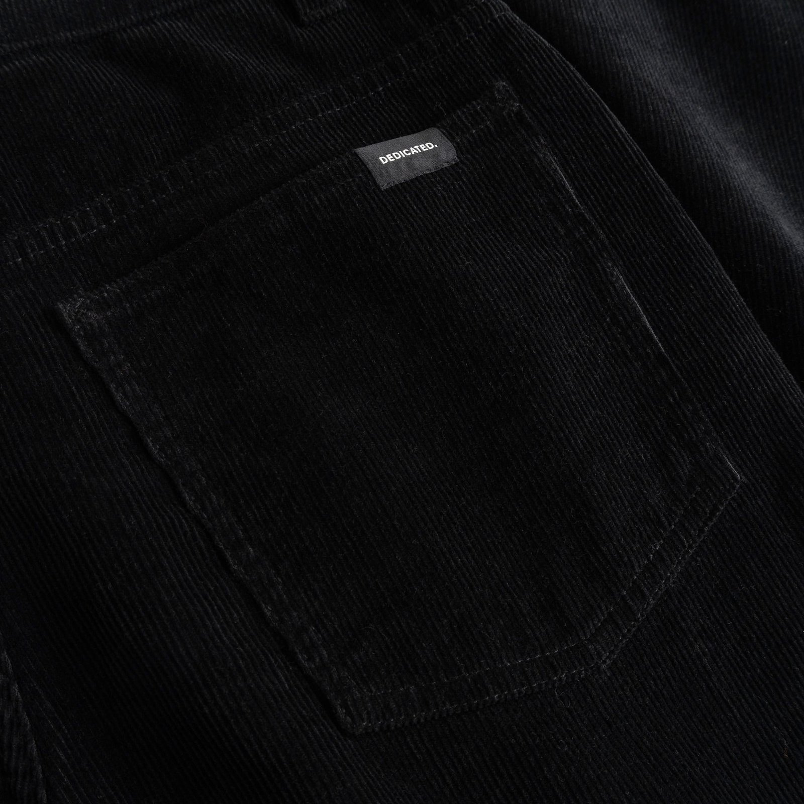 Nahaufnahme der Gesäßtasche der schwarzen Cordhose Ryda. Zu sehen sind die Cordstruktur und das kleine Dedicated-Markenlabel.