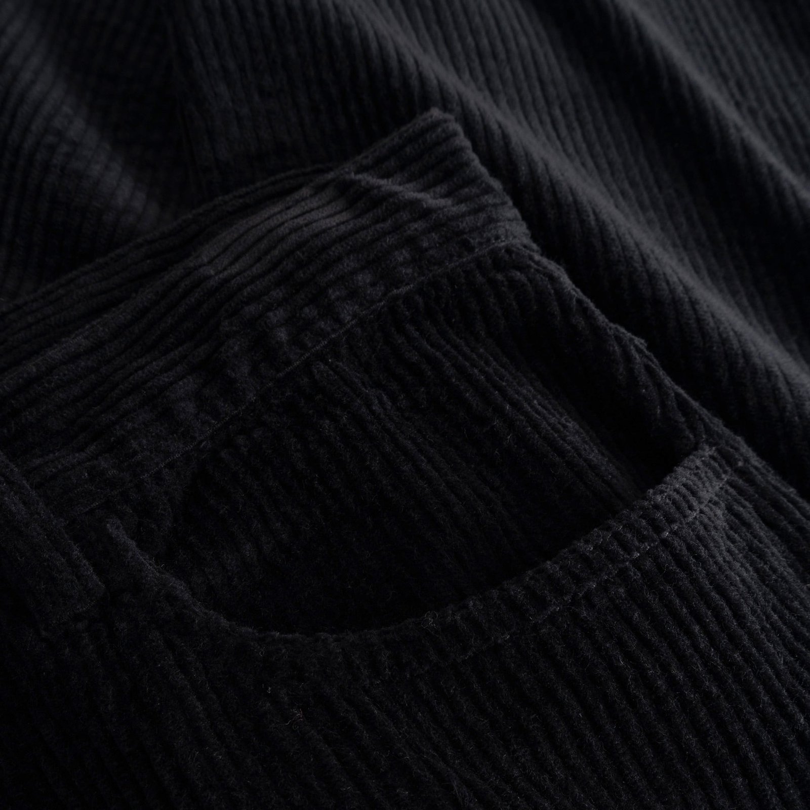 A close-up view of the rich, ribbed corduroy fabric and front pocket of the black Hamburg pants.