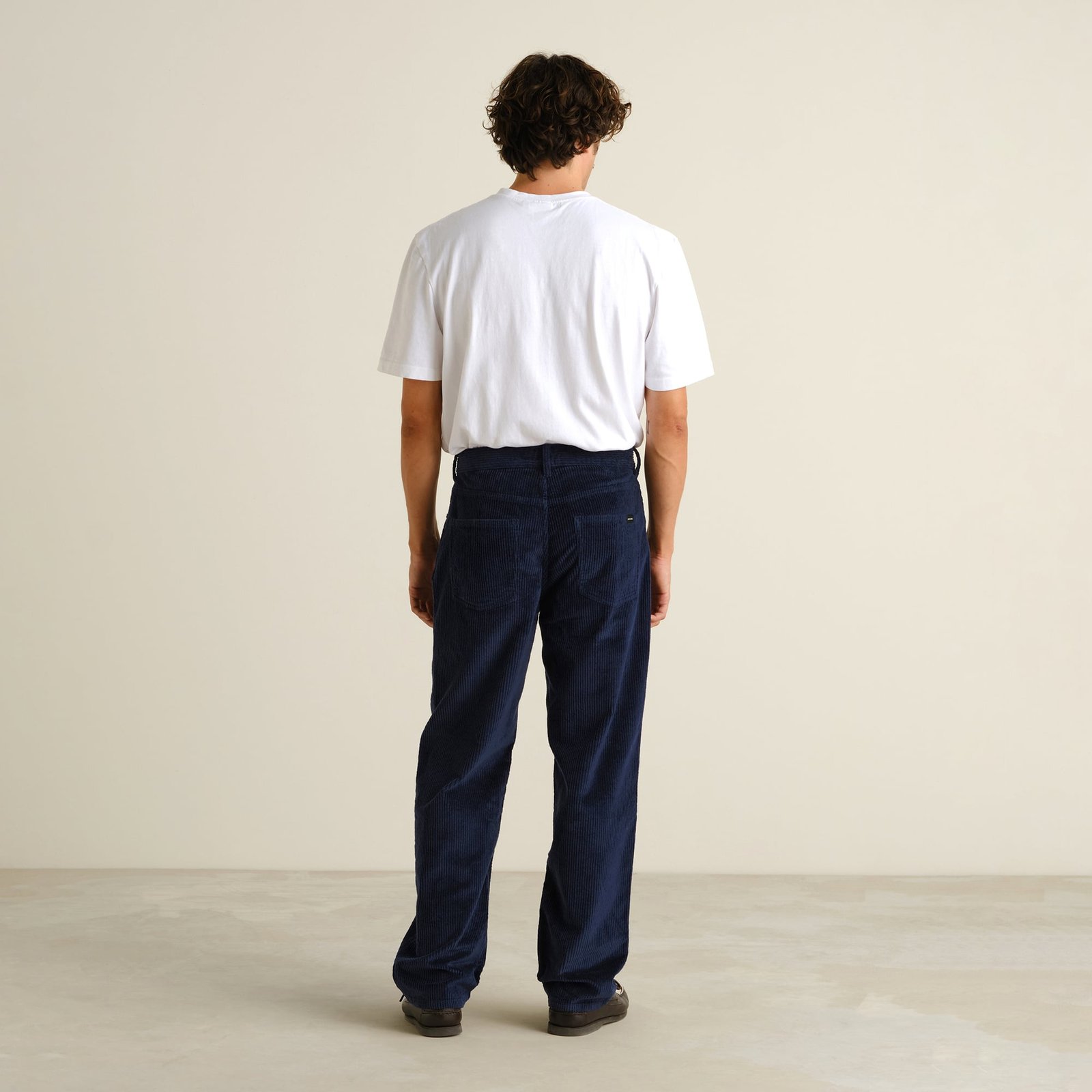 Man seen from behind wearing the relaxed-fit Hamburg Corduroy Pants in navy with a simple white tee.