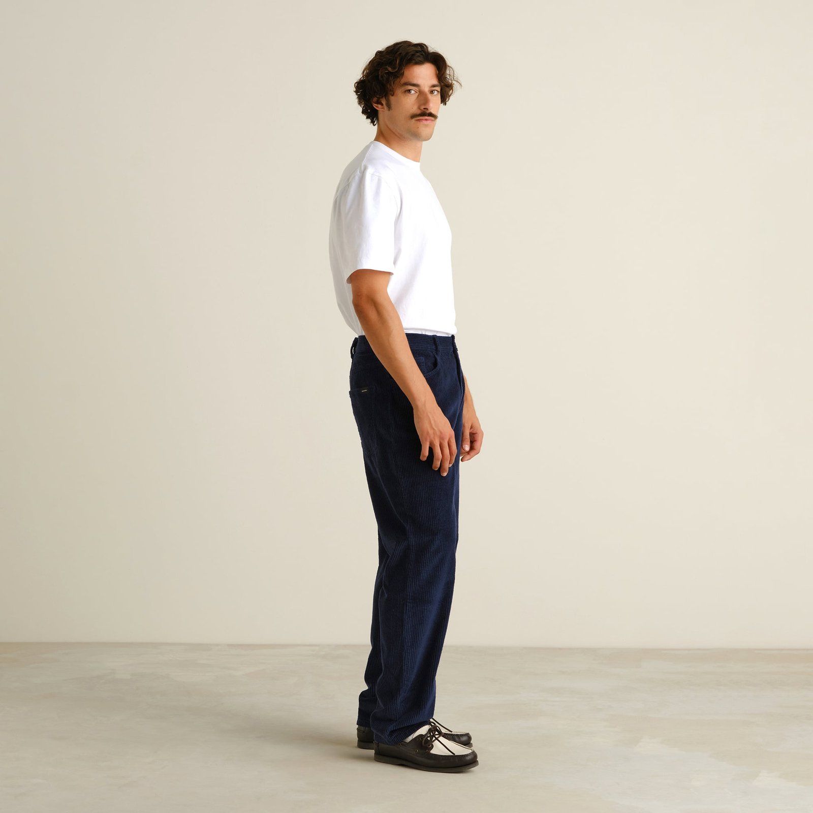 Side profile of a model wearing the relaxed-fit Pants Hamburg Corduroy in Navy with a white t-shirt.