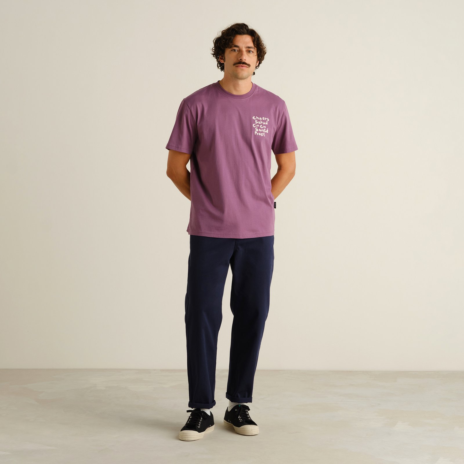 A man styles the navy Chino Pants Hudiksvall with a purple graphic tee and classic sneakers for a relaxed, everyday look.
