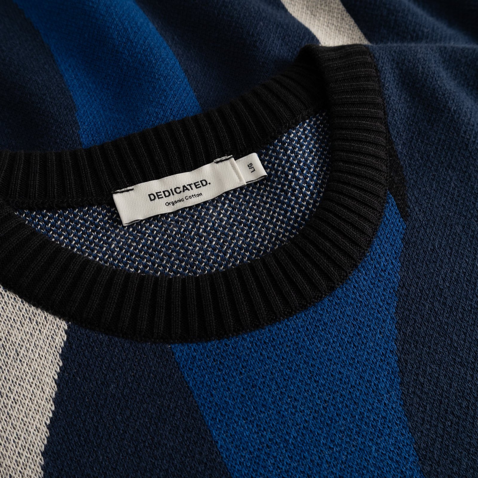 Detail shot of the Sweater Mora Wavy Stripe Blue showing the jacquard knit, ribbed black collar, and Dedicated label.