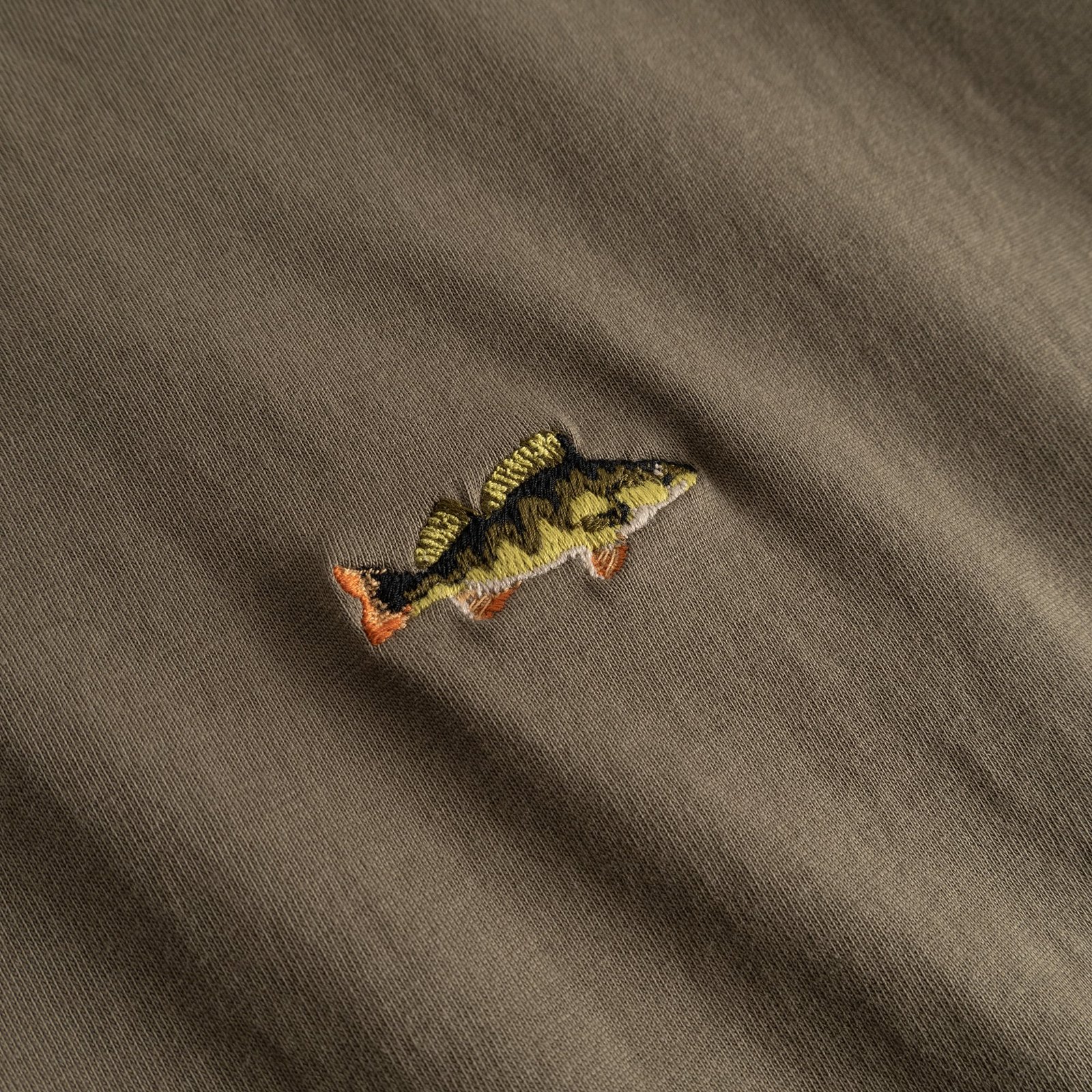 A detailed close-up of the perch fish embroidery on the T-shirt Stockholm in Bungee Green.