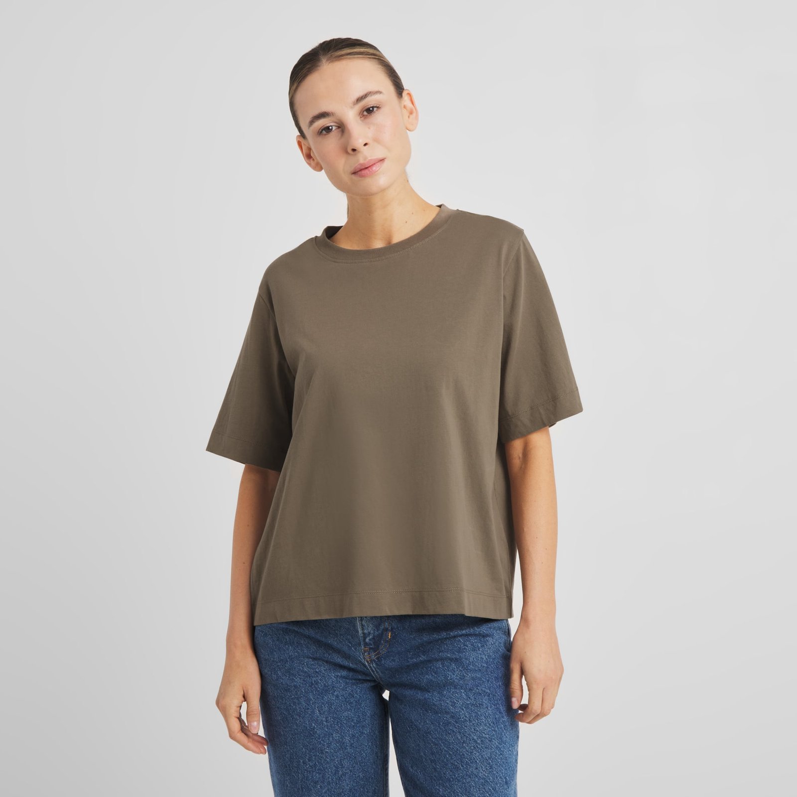 Front view of a woman wearing the T-shirt Vadstena Base in Bungee Green with a pair of classic blue jeans.