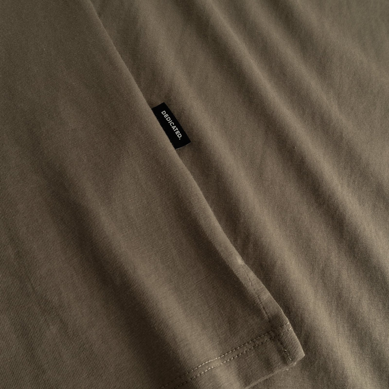 Detailed shot of the soft, bungee green fabric of the Visby T-shirt, with the classic Dedicated label on the side seam.
