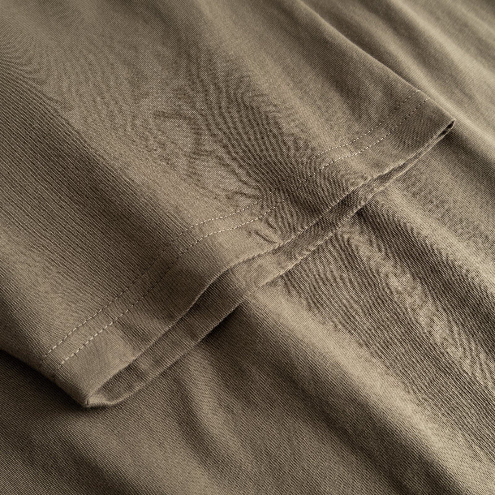 Närbild på ärmen på T-shirt Stockholm Base i Bungee Green, som visar de fina sömmarna och det mjuka bomullstyget.