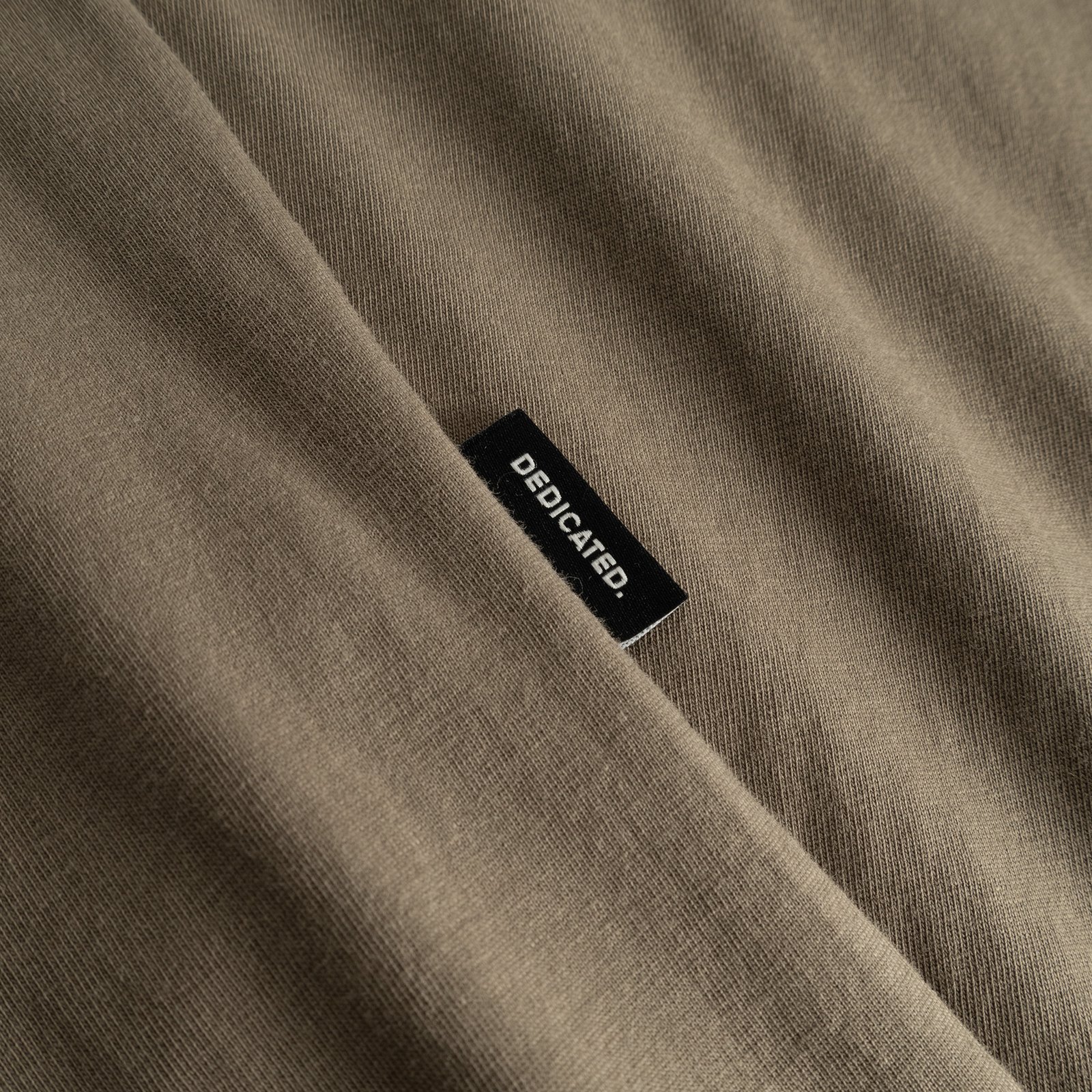 Närbild på det Bungee Green-färgade tyget och Dedicateds svarta etikett på T-shirt Stockholm Base.