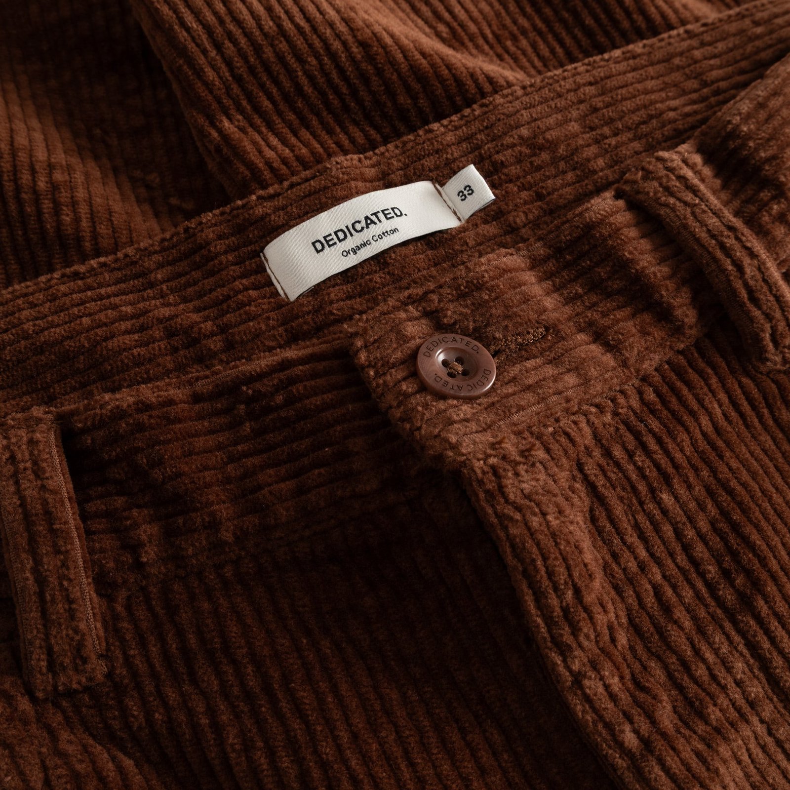 A close-up of the brown corduroy fabric on the Pants Hamburg, showing the DEDICATED brand label at the waistband.