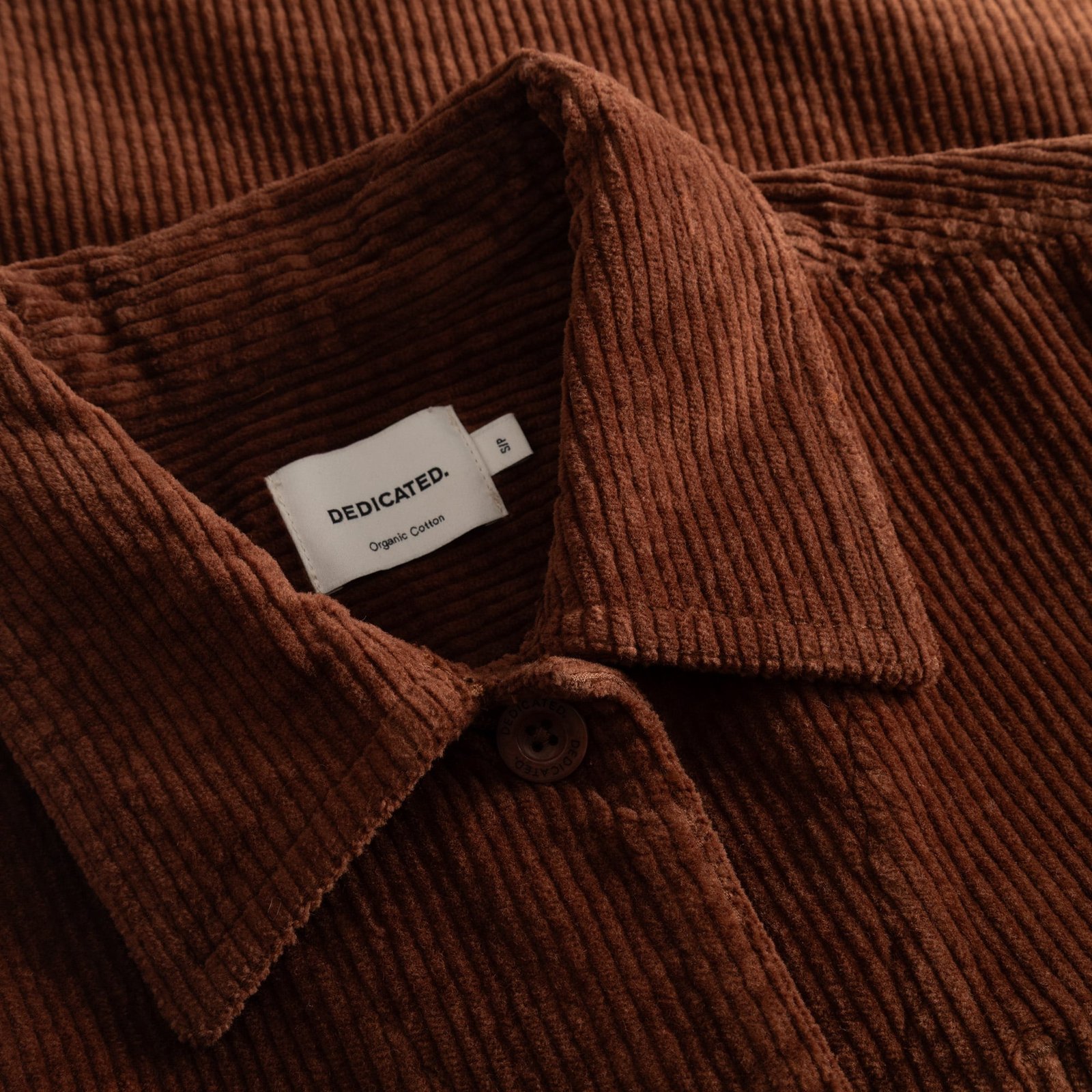 A close-up of the soft, ribbed texture of the Stiby Corduroy Jacket in Cappuccino Brown, featuring the Dedicated brand label.
