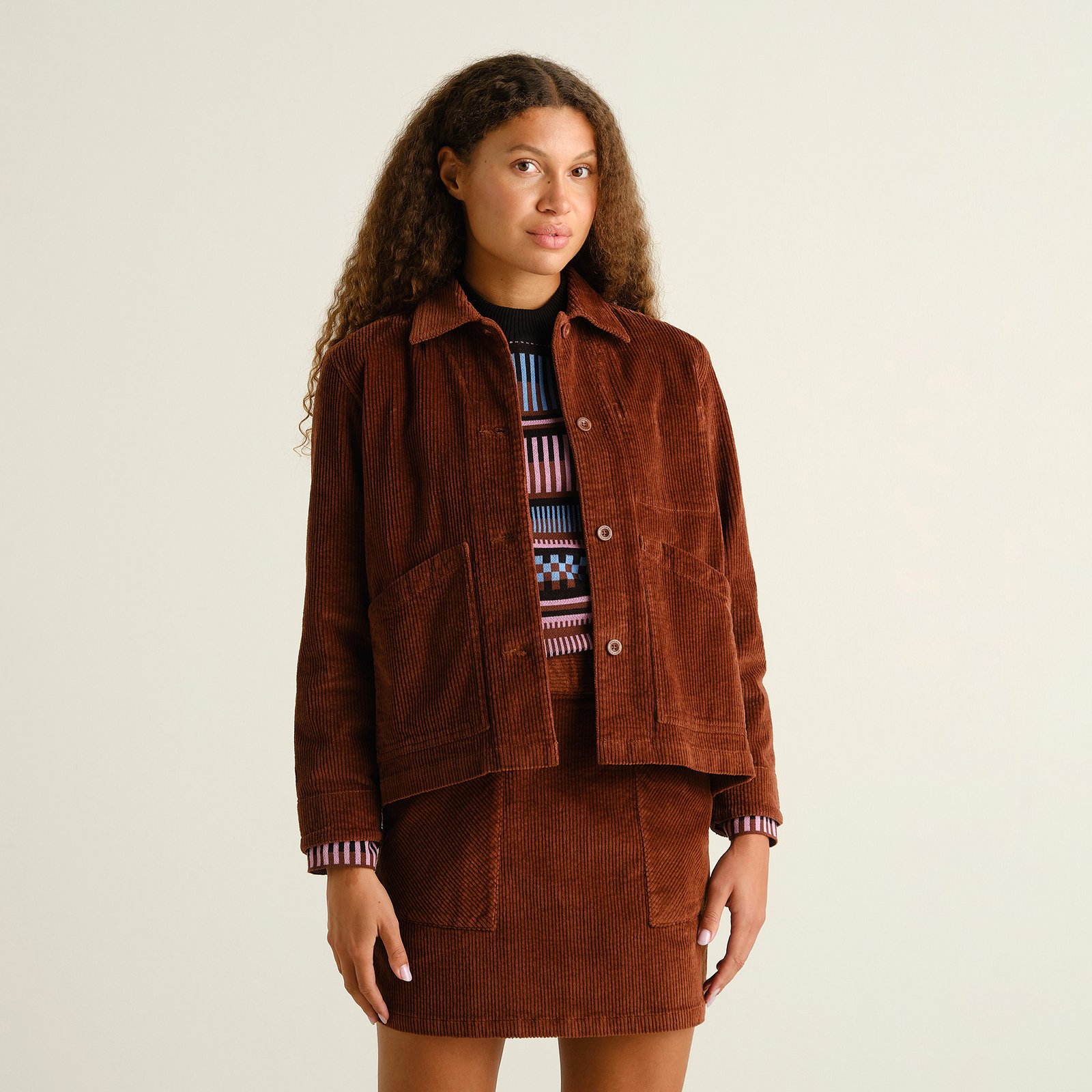 Woman with curly hair styles the Stiby Corduroy Jacket in Cappuccino Brown with a matching mini skirt for a cool co-ord look.