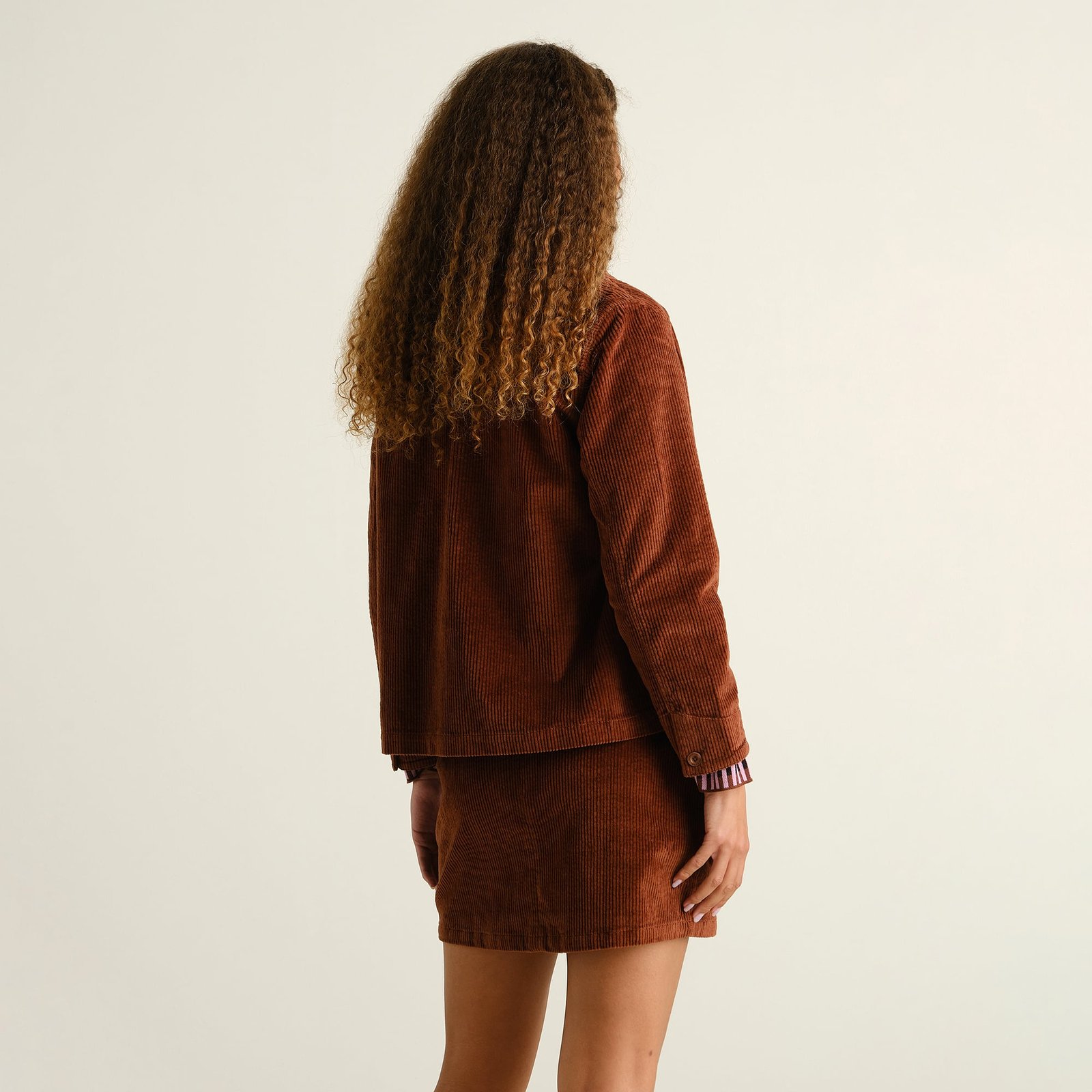 Back view of a model with long curly hair, styling the Skirt Majorna Corduroy in Cappuccino Brown with a matching jacket.
