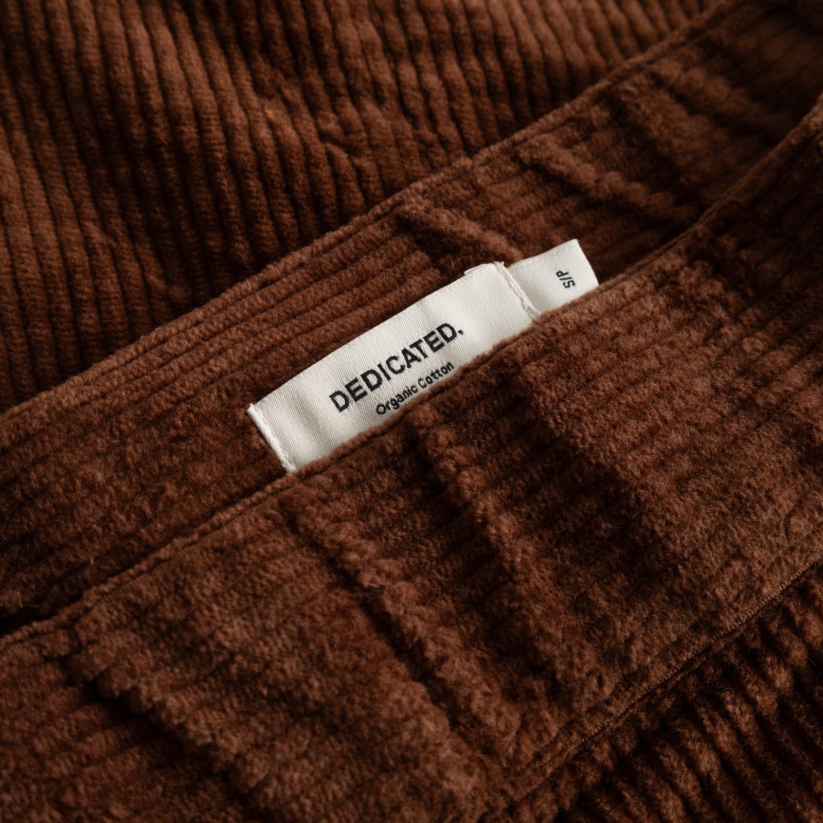 Close-up of the rich brown corduroy fabric of the Skirt Majorna, showing the white Dedicated brand label.