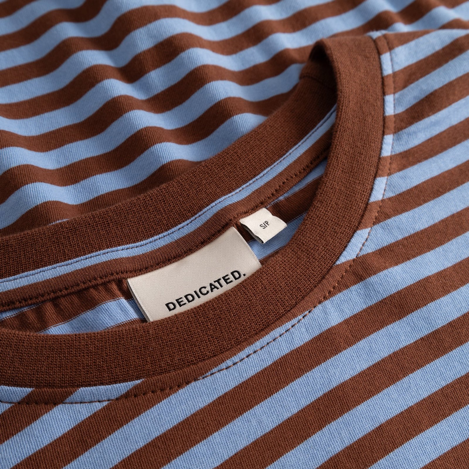 A close-up shot of the Vadstena t-shirt, highlighting its brown and blue stripes and the soft ribbed collar.