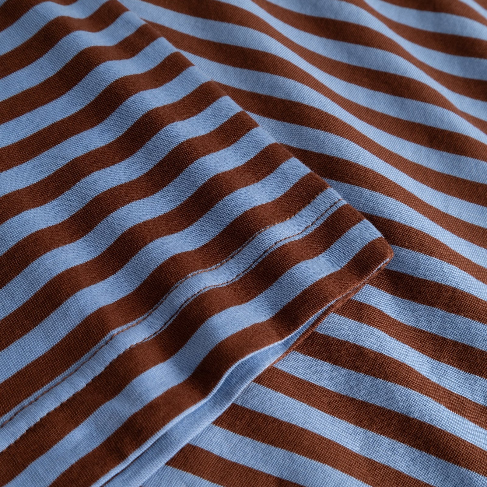 Close-up detail shot of the T-shirt Vadstena, showing the soft striped fabric in cappuccino brown and cornflower blue.