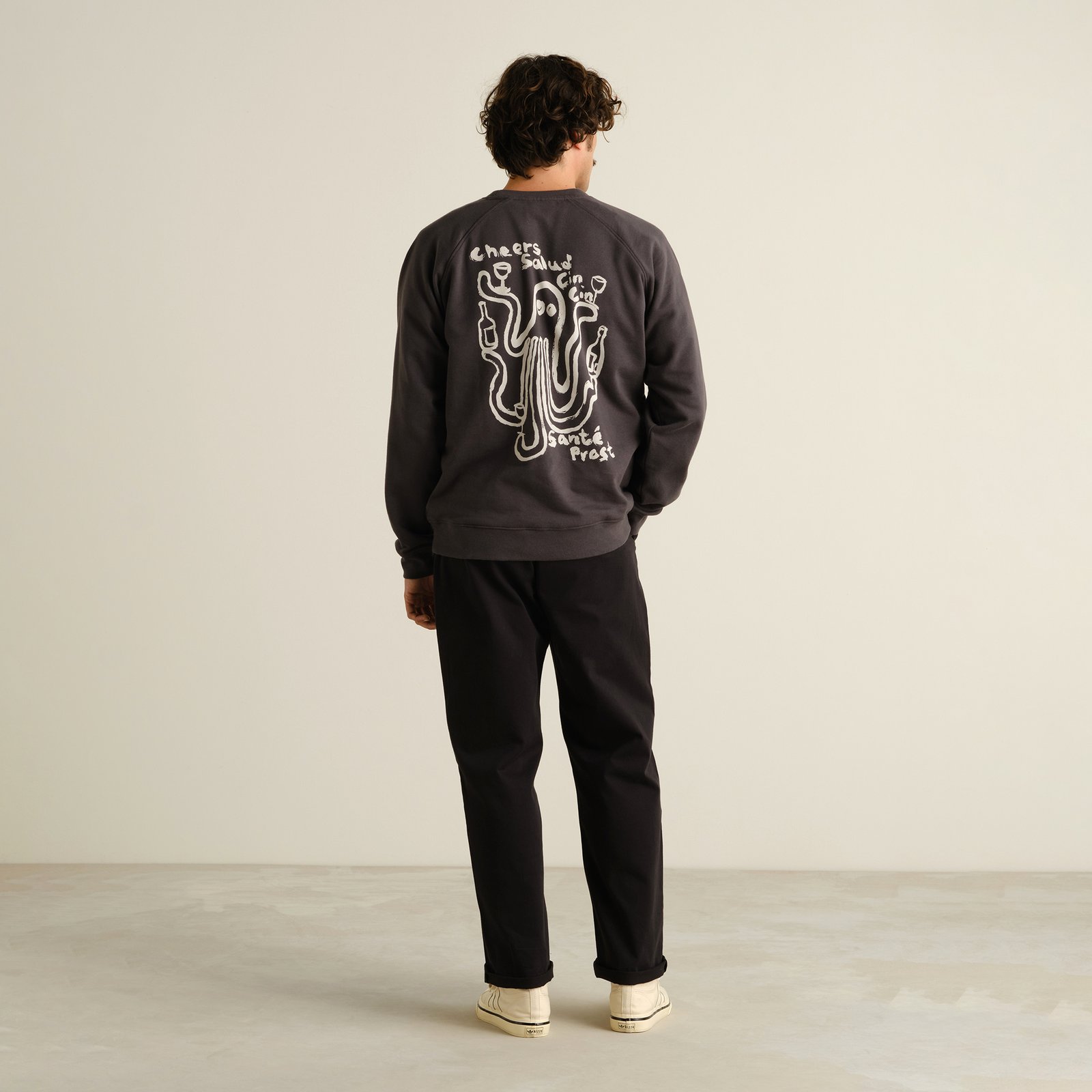 Back shot of a model wearing the versatile black Hudiksvall Chino Pants, styled with a graphic sweater and sneakers.