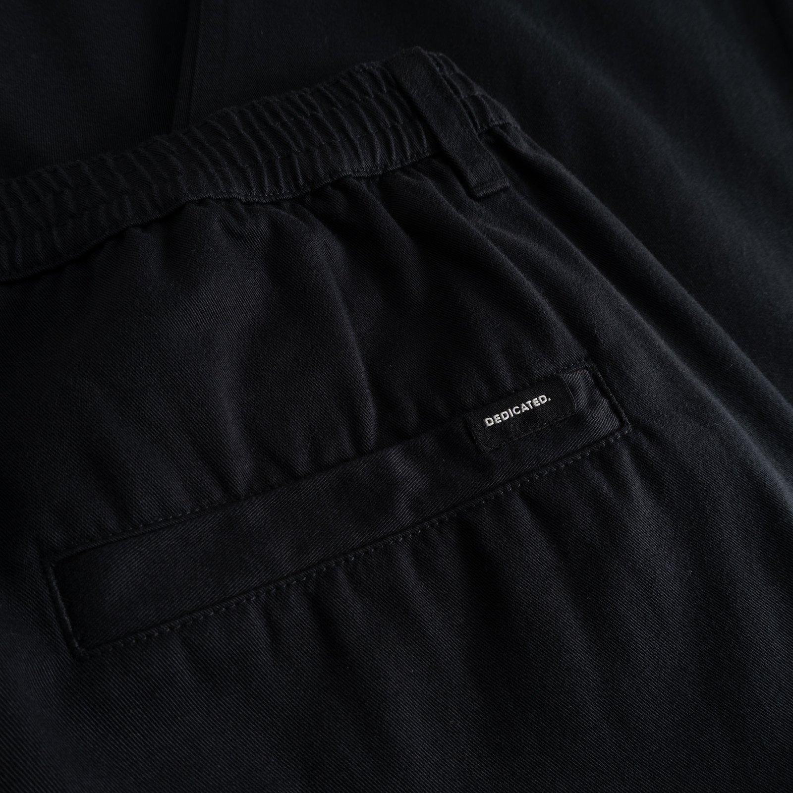 A detailed look at the comfy elastic waistband and back welt pocket of the black Hudiksvall Chino Pants.