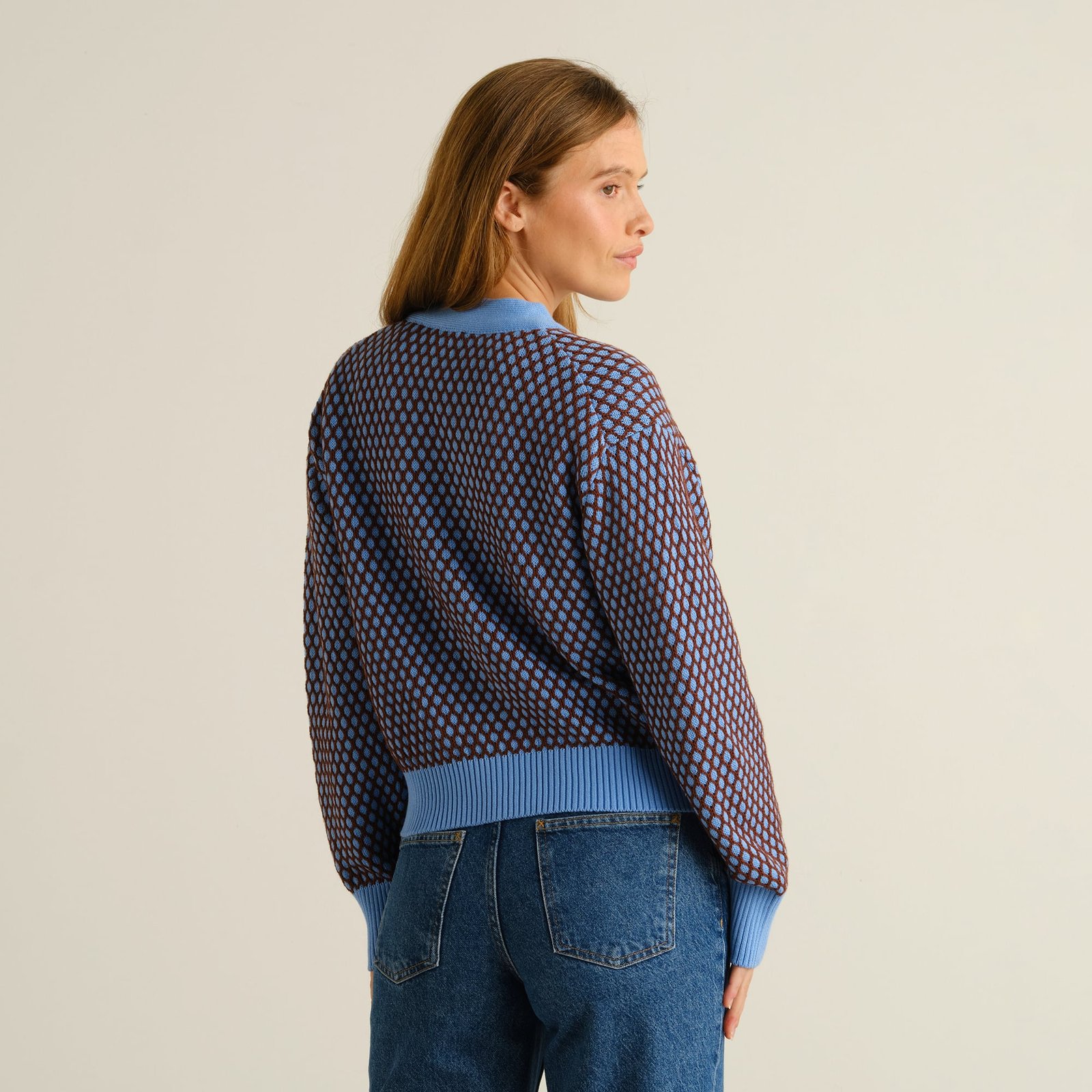 Baksidan av en modell som bär Kanan Bubble Knit Cardigan i blåklintsblått och cappuccinobrunt, tillsammans med blåjeans.