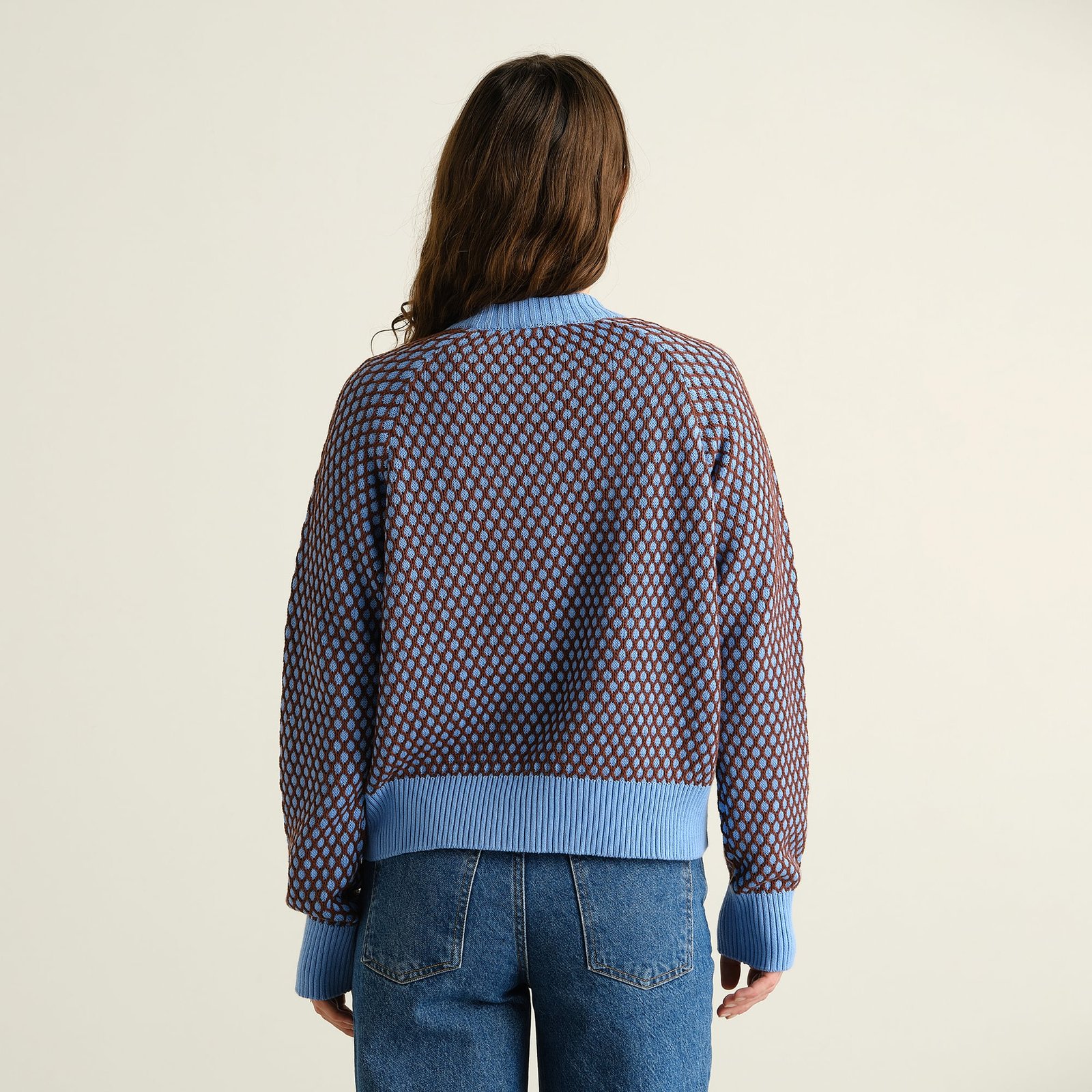 Baksidan av en kvinna som bär den stickade tröjan Husie Bubble Knit i blått och brunt med blå jeans.