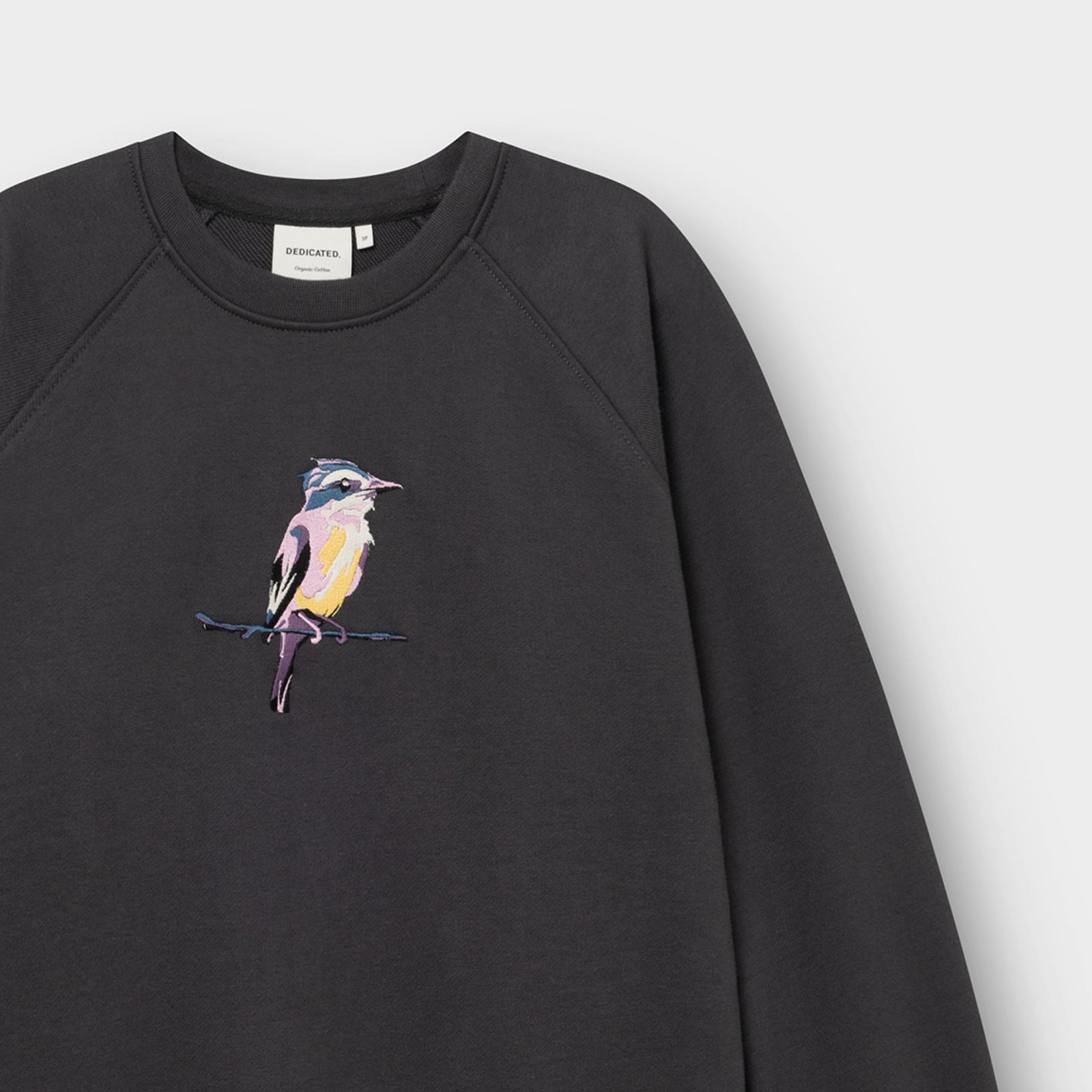 Close-up of the charcoal Ystad sweatshirt, showing the colorful painted bird embroidery, crew neck, and Dedicated label.