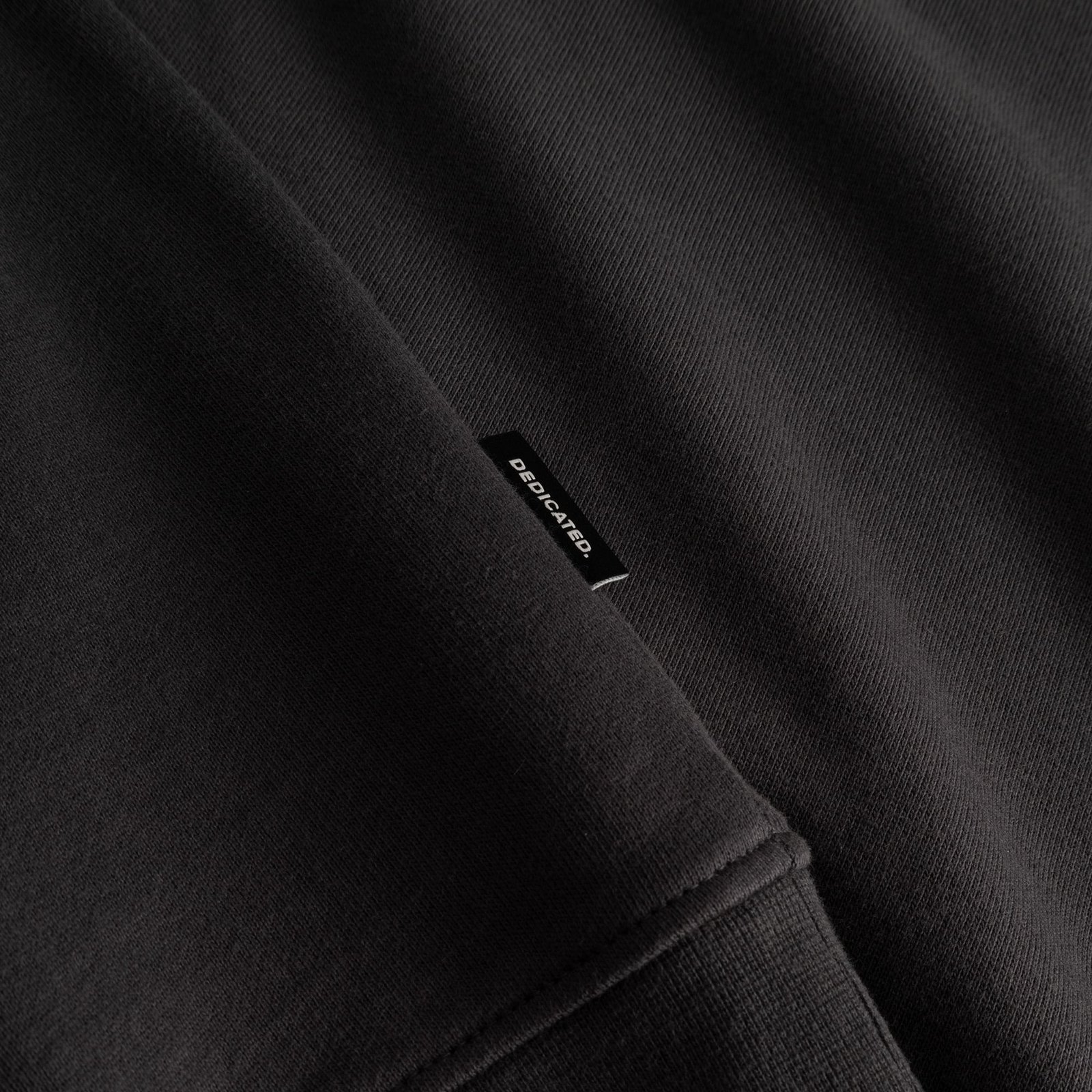 A detailed shot of the charcoal Ystad sweatshirt's ribbed hem, with the discreet black Dedicated logo tab neatly stitched in.