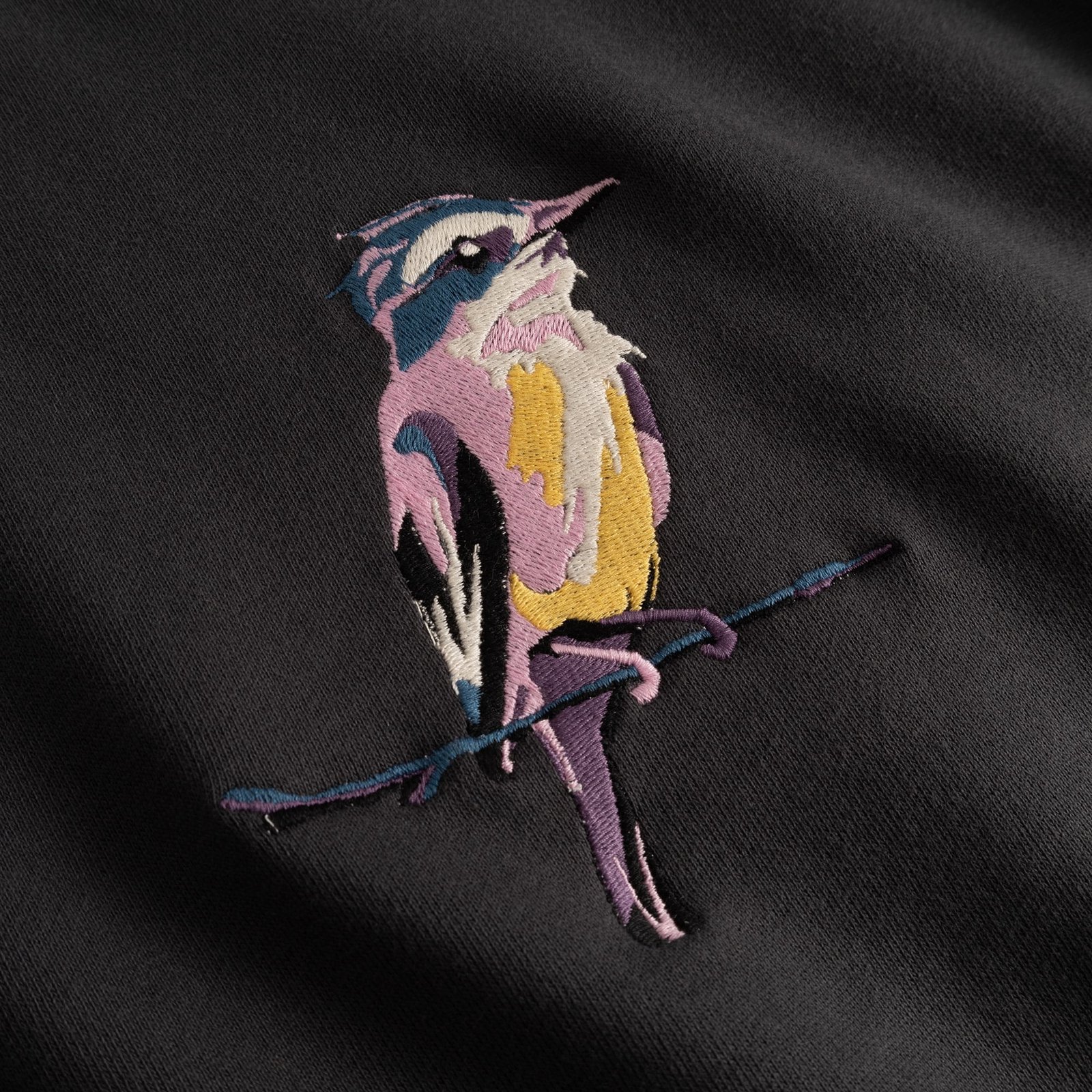 A detailed close-up of the Ystad Sweatshirt shows off the vibrant 'Painted Bird' embroidery in stunning detail.
