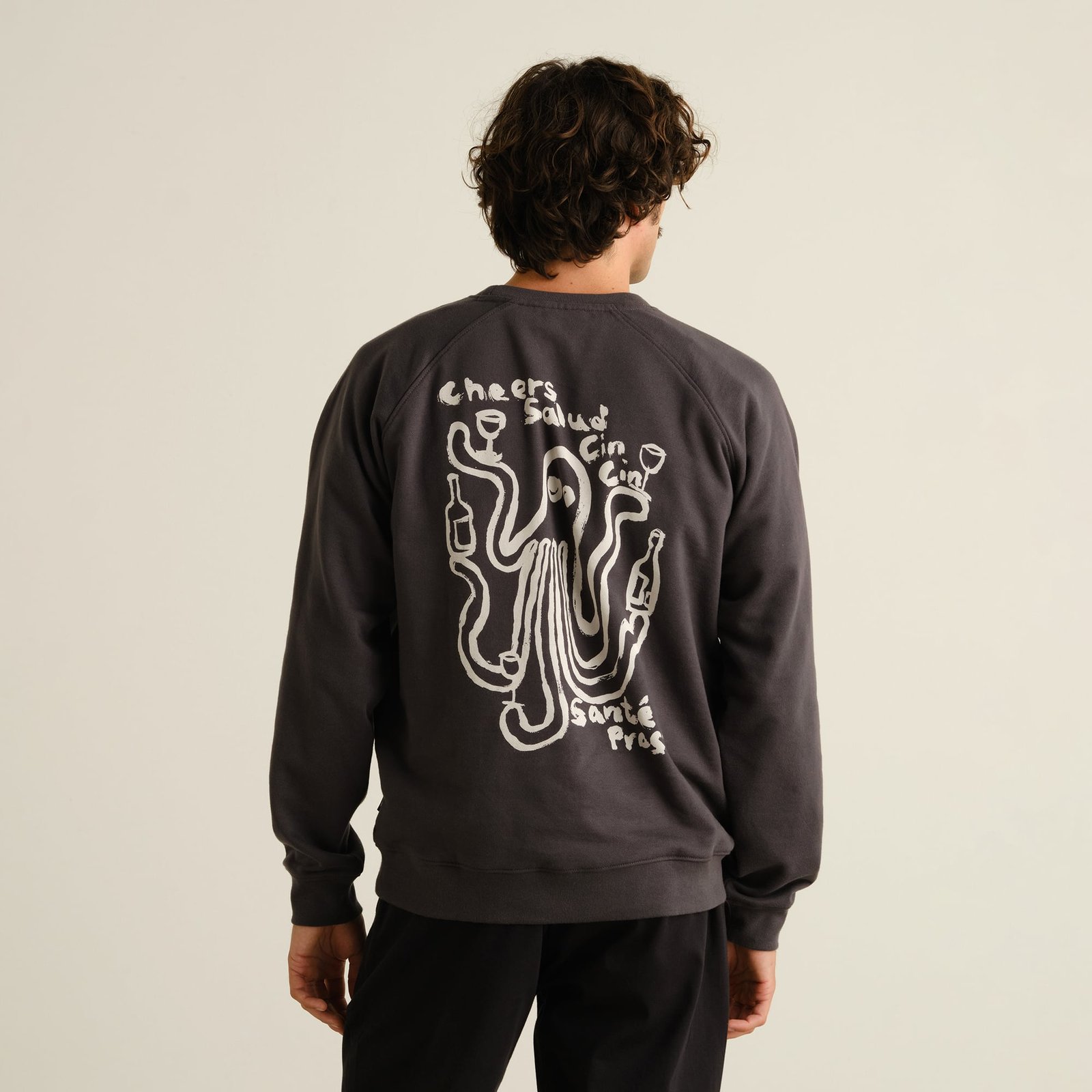 Model seen from behind wearing a charcoal grey sweatshirt with a playful white graphic of an octopus toasting with wine.
