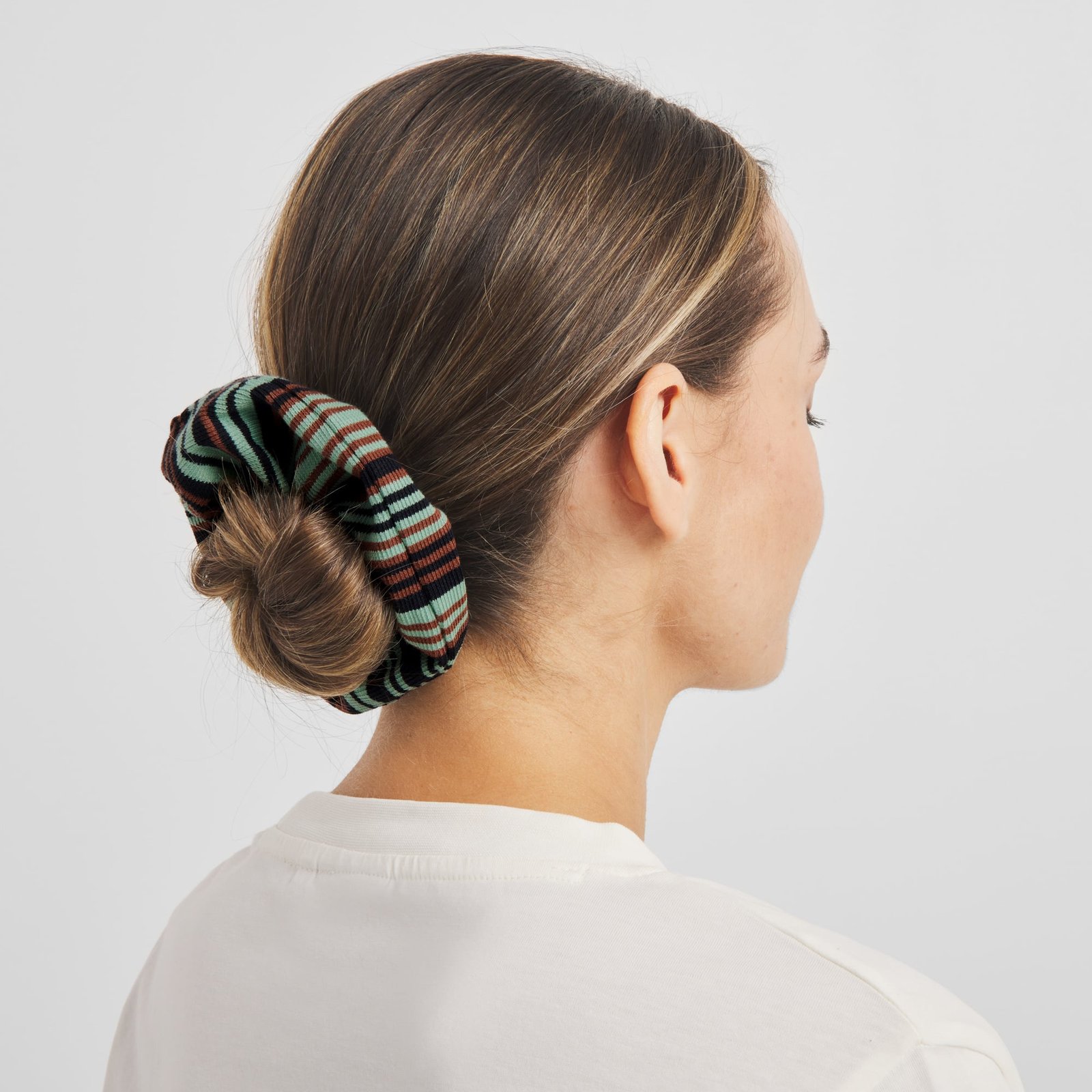 A model styles a neat low bun with the colorful Scrunchie Irregular Stripe Green.