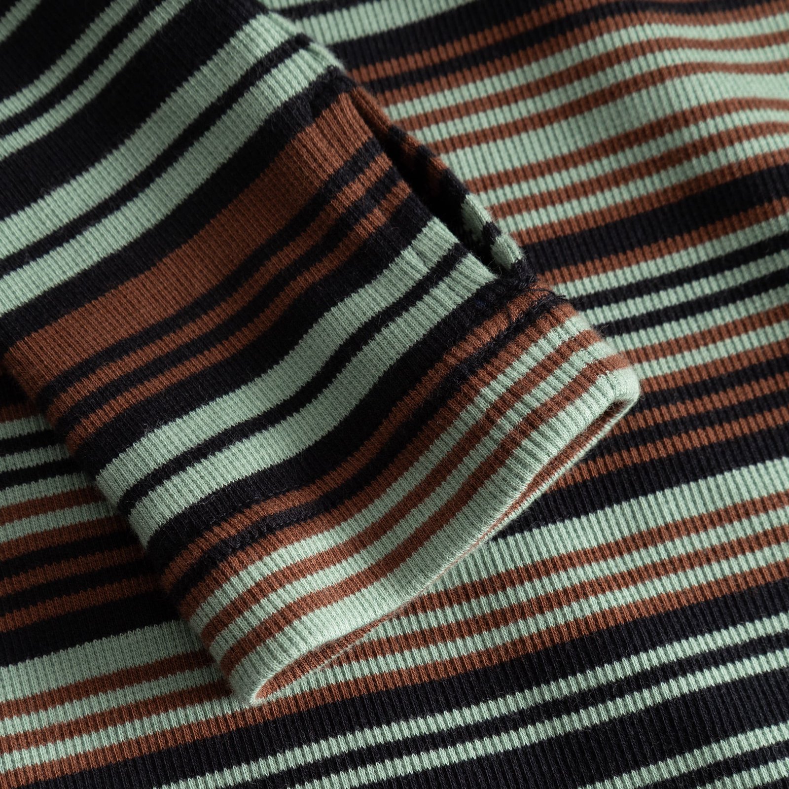Close-up of the Rib Top Malma sleeve, highlighting the thumbhole detail and the soft, ribbed irregular stripe fabric.